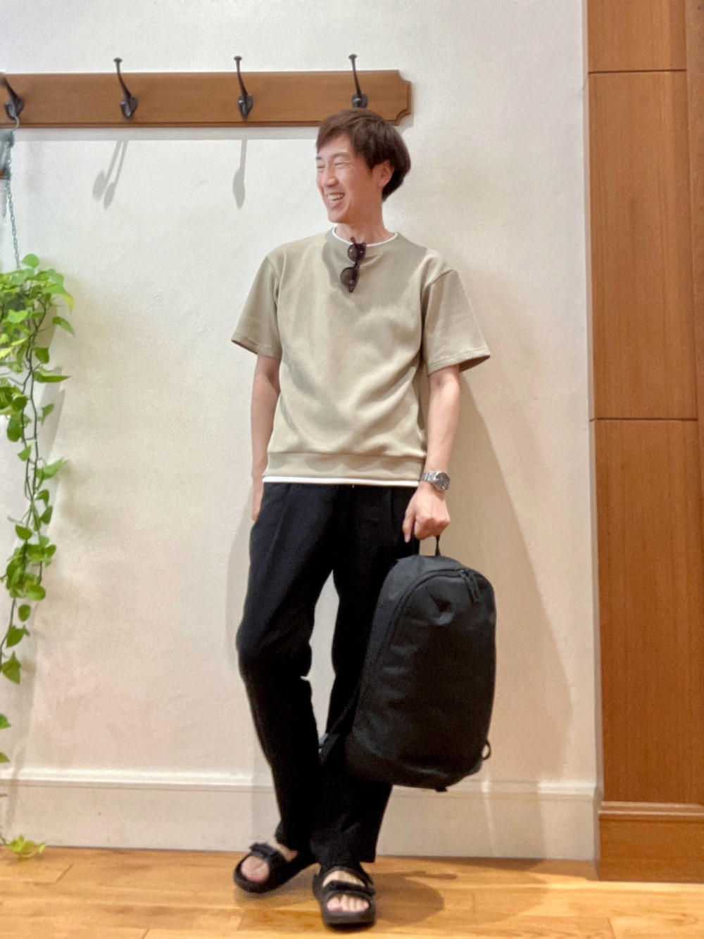ブラック系のバックパック/リュック、ベージュ系のTシャツ/カットソー、ブラック系のサンダルを着用したメンズの夏コーディネートの1枚目の写真