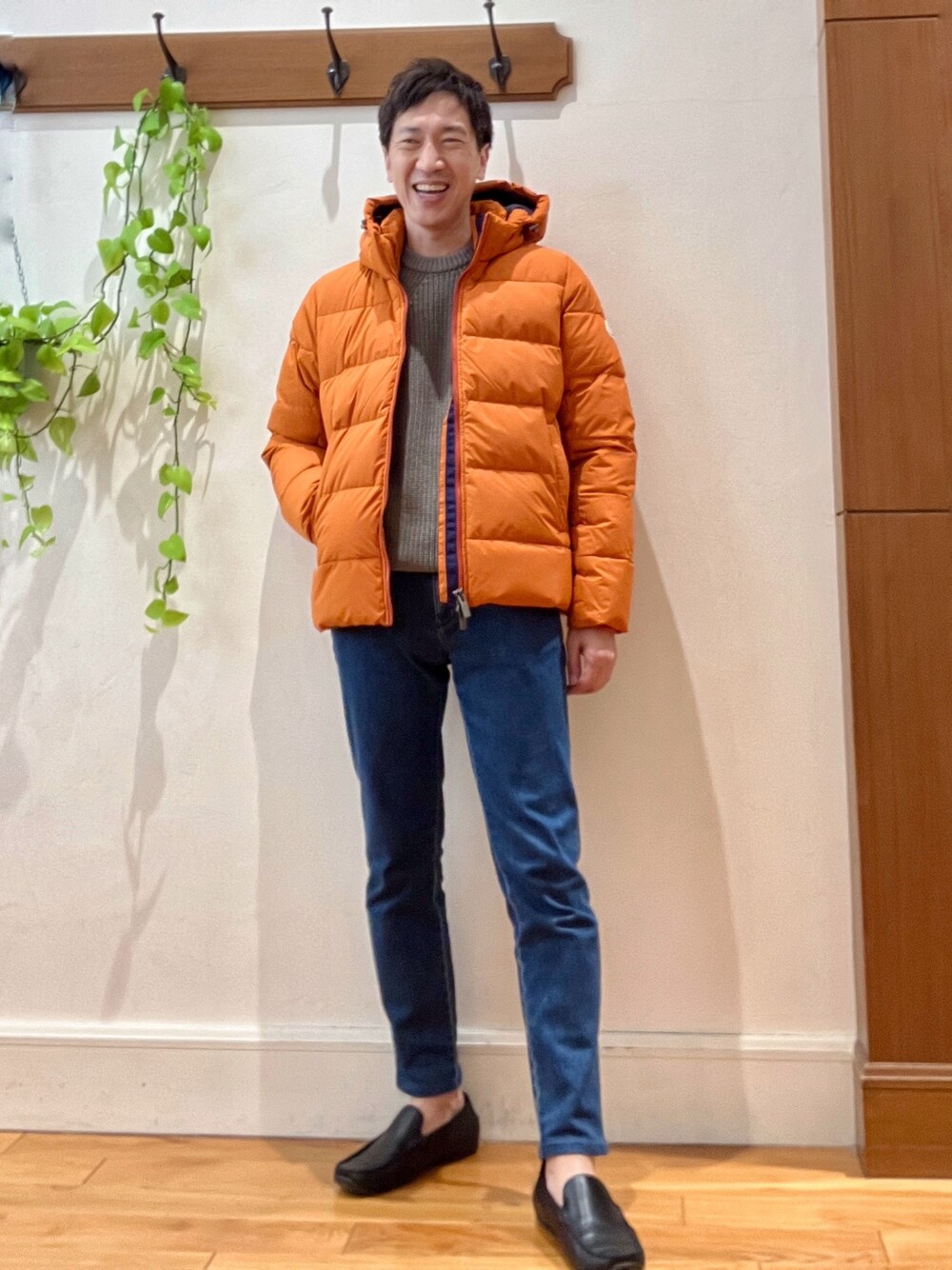 ブルー系のデニムパンツ、ベージュ系のニット/セーター、オレンジ系のダウンジャケット/コートを着用したメンズの冬コーディネートの1枚目の写真