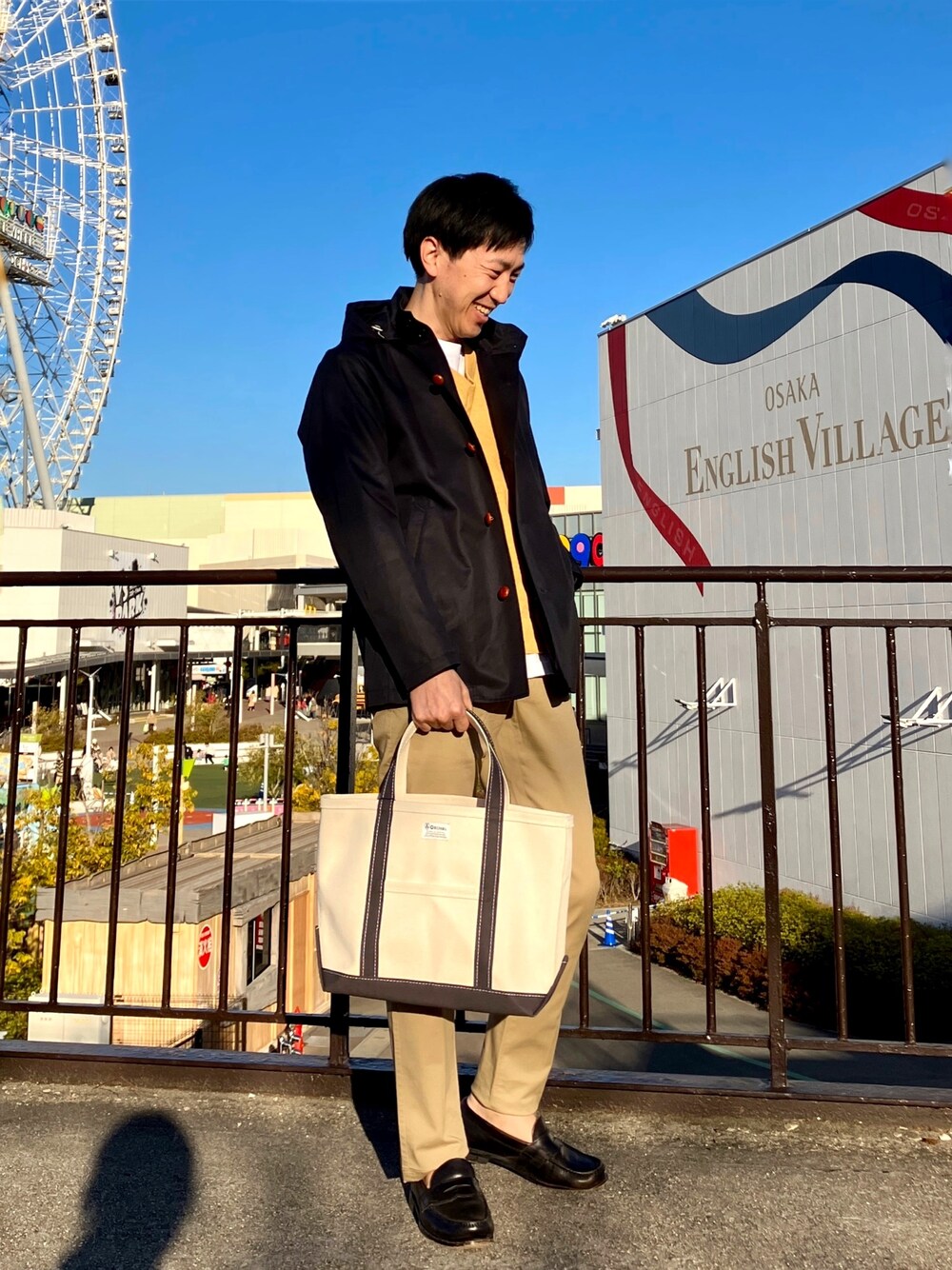 ブルー系のブルゾン、ホワイト系のトートバッグ、ベージュ系のチノパンツを着用したメンズの春コーディネートの1枚目の写真