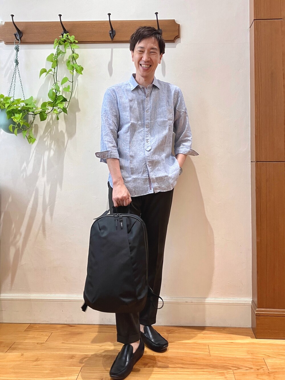 ブルー系のシャツ/ブラウス、ブラウン系のスラックス、ブラック系のバックパック/リュックを着用したメンズの春コーディネートの1枚目の写真