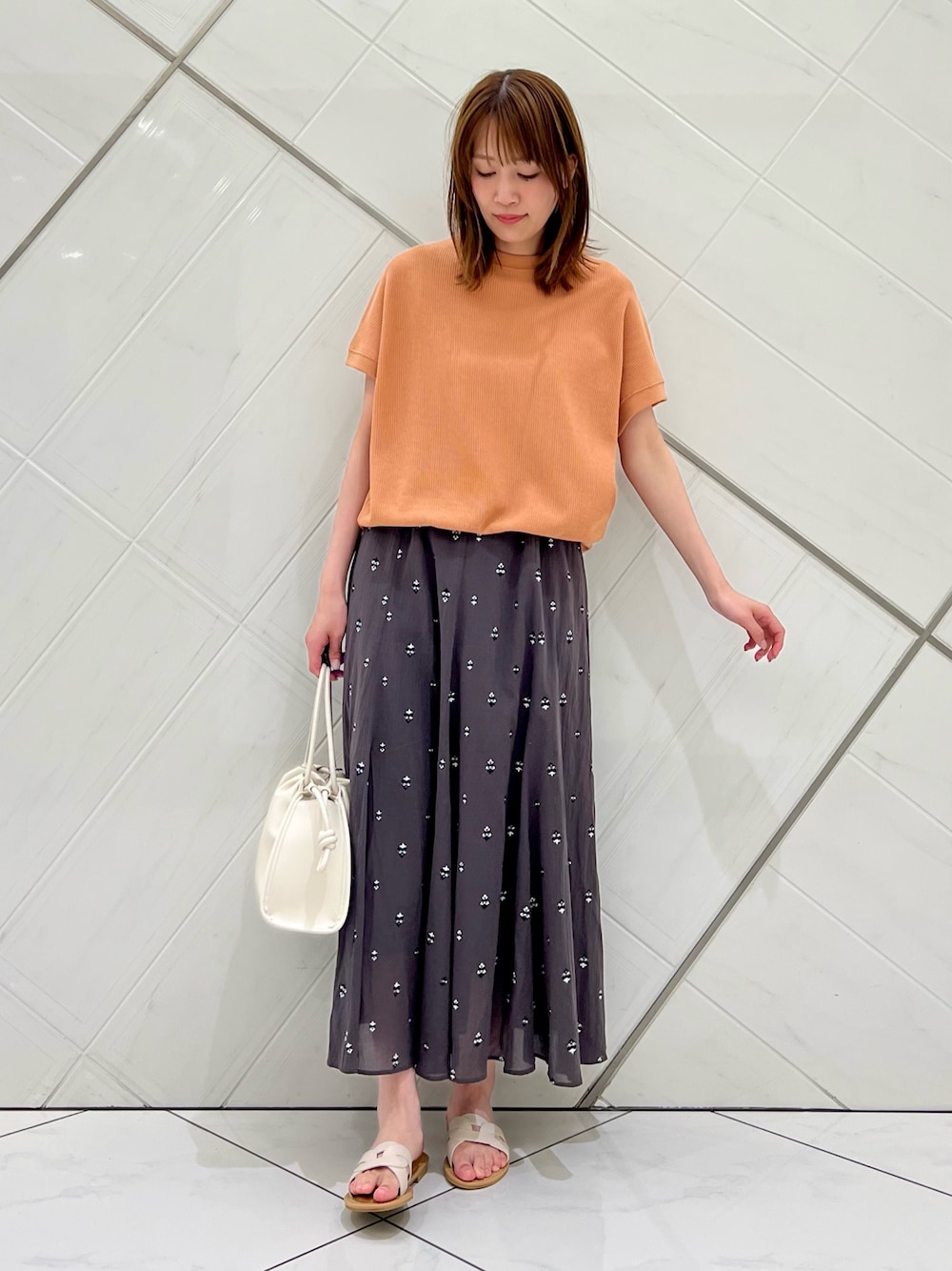 レッド系のTシャツ/カットソー、グレー系のスカート、ホワイト系のトートバッグを着用したレディースの春コーディネートの1枚目の写真