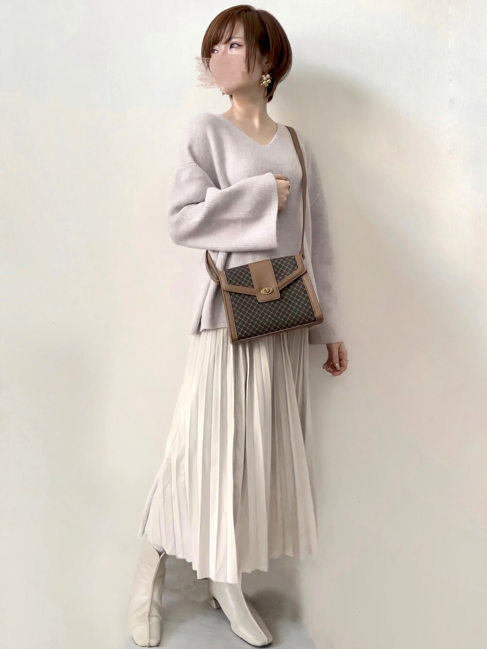 グレー系のニット/セーター、ブラウン系のショルダーバッグ、ホワイト系のスカートを着用したレディースの春コーディネートの1枚目の写真