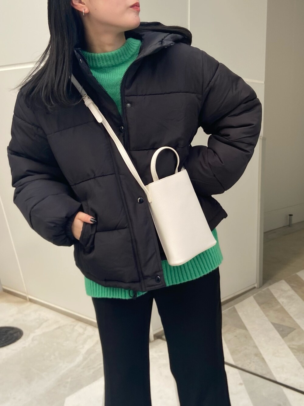 ホワイト系のショルダーバッグ、ブラック系のダウンジャケット/コート、グリーン系のカーディガン/ボレロを着用したレディースの冬コーディネートの2枚目の写真