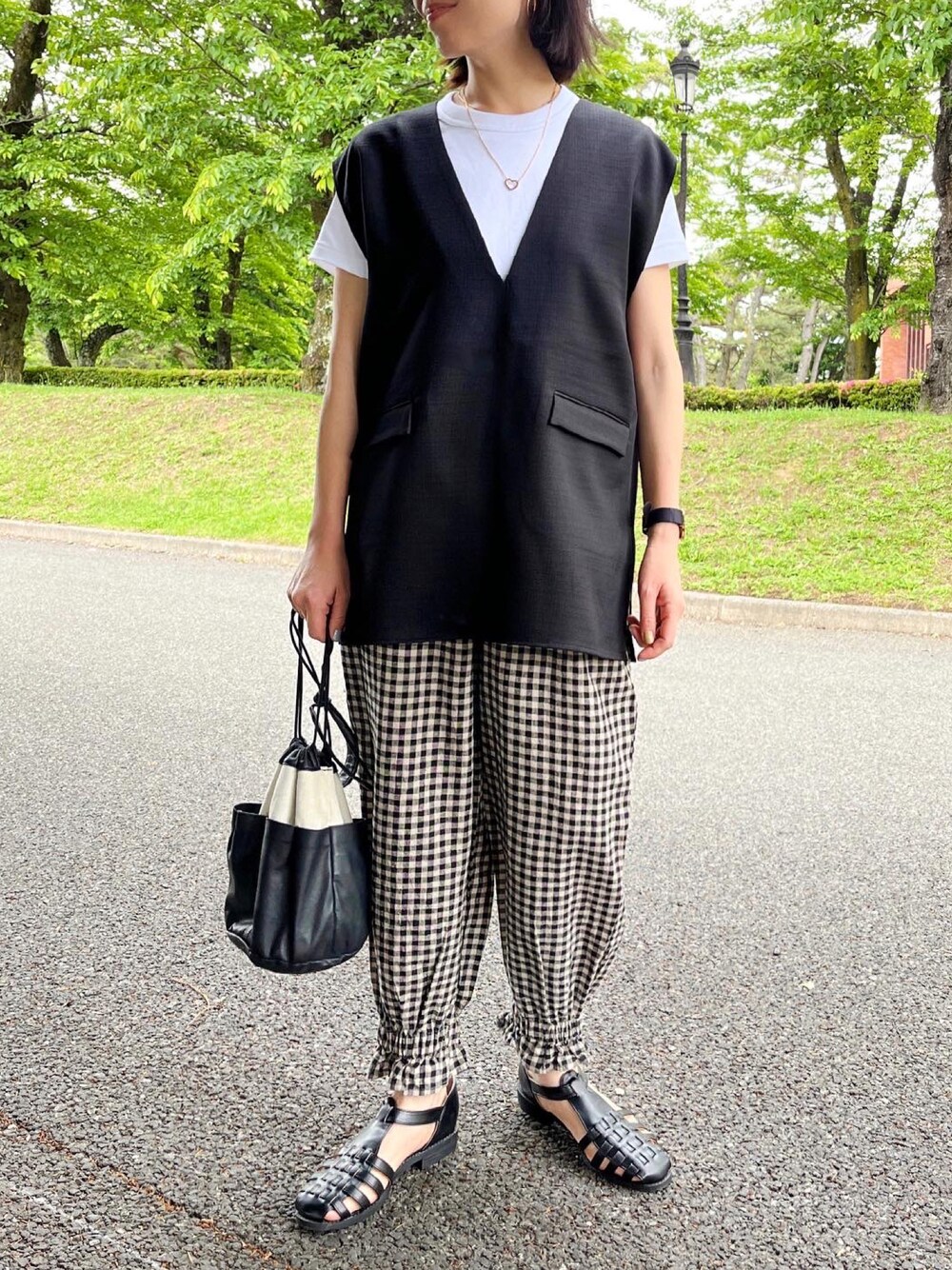 ブラック系のベスト、ホワイト系のパンツ、ブラック系のサンダルを着用したレディースの春コーディネートの1枚目の写真