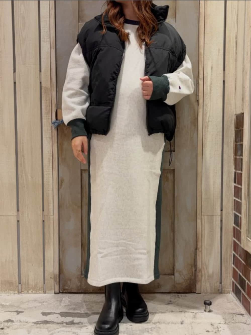 ブラック系のブーツ、ブラック系のダウンベスト、ベージュ系のワンピースを着用したレディースの冬コーディネートの1枚目の写真