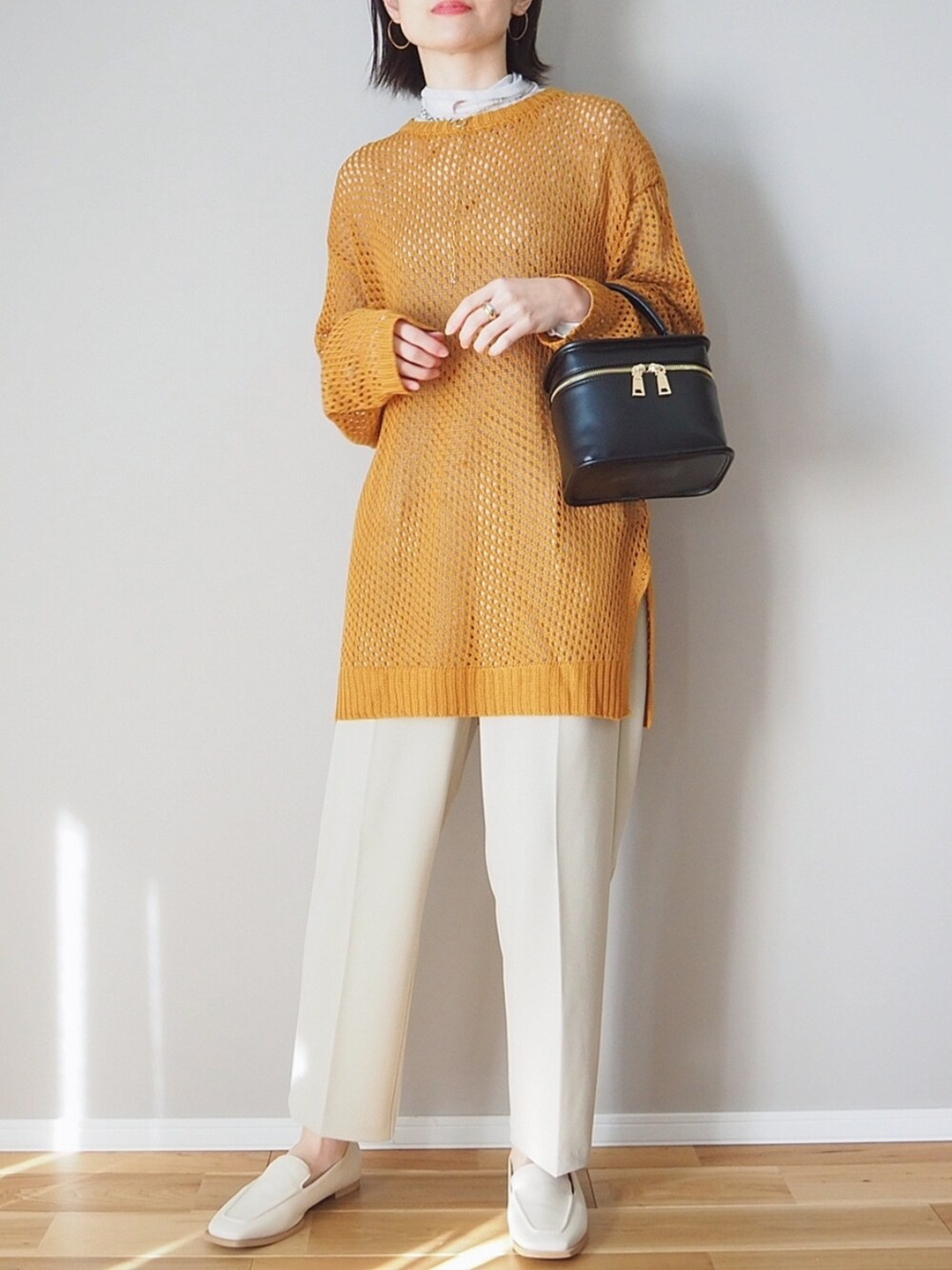 オレンジ系のニット/セーター、ベージュ系のスラックス、ブラック系のショルダーバッグを着用したレディースの冬コーディネートの2枚目の写真