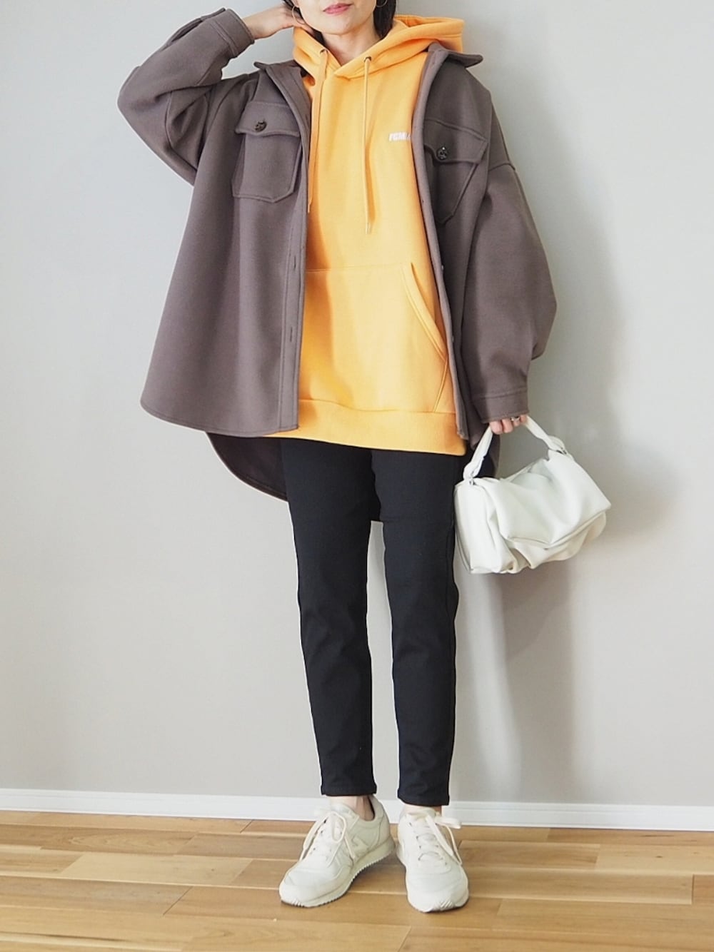 オレンジ系のパーカー、ブラック系のデニムパンツ、ブラウン系のカバーオールを着用したレディースの春コーディネートの2枚目の写真