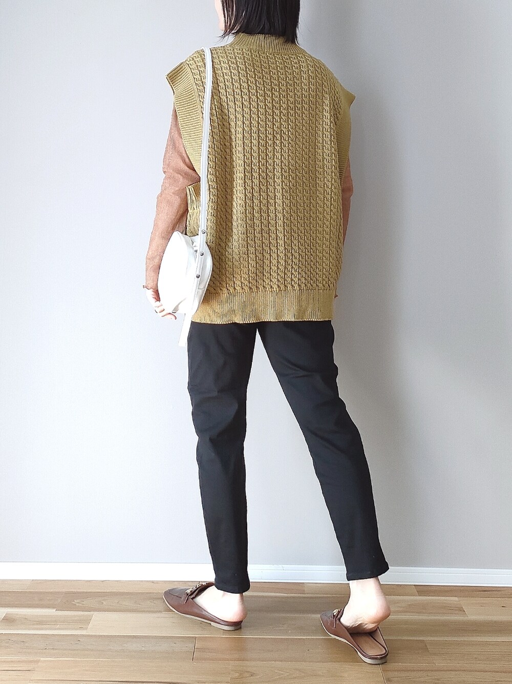 イエロー系のベスト、ブラック系のデニムパンツ、ホワイト系のショルダーバッグを着用したレディースの春コーディネートの3枚目の写真