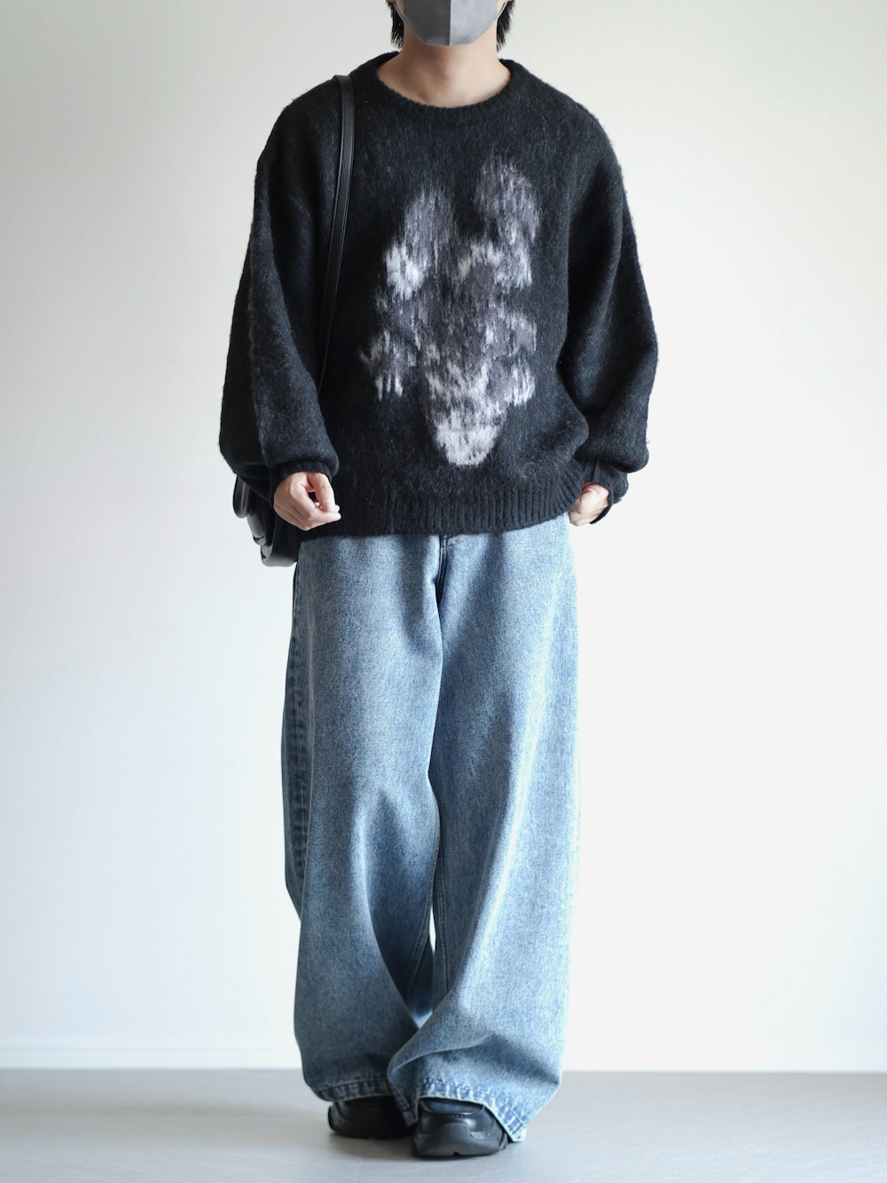 ブラック系のショルダーバッグ、ブラック系のニット/セーター、ブルー系のデニムパンツを着用したメンズの秋コーディネートの1枚目の写真