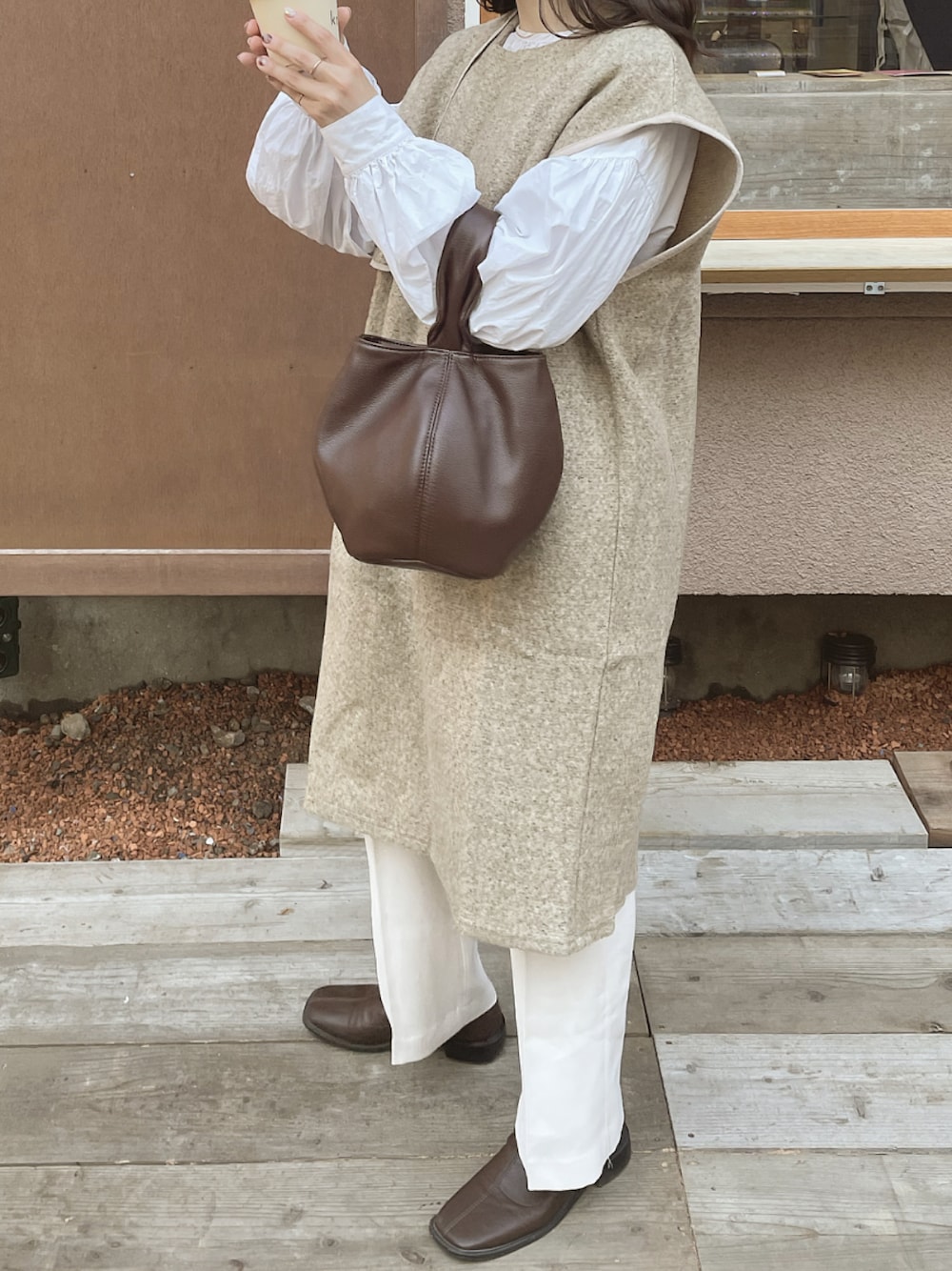 ベージュ系のベスト、ブラウン系のハンドバッグ、ホワイト系のシャツ/ブラウスを着用したレディースの冬コーディネートの1枚目の写真