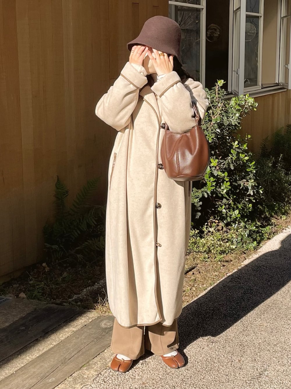 ブラウン系のハンドバッグ、ベージュ系のノーカラーコート、ブラウン系のスラックスを着用したレディースの冬コーディネートの1枚目の写真