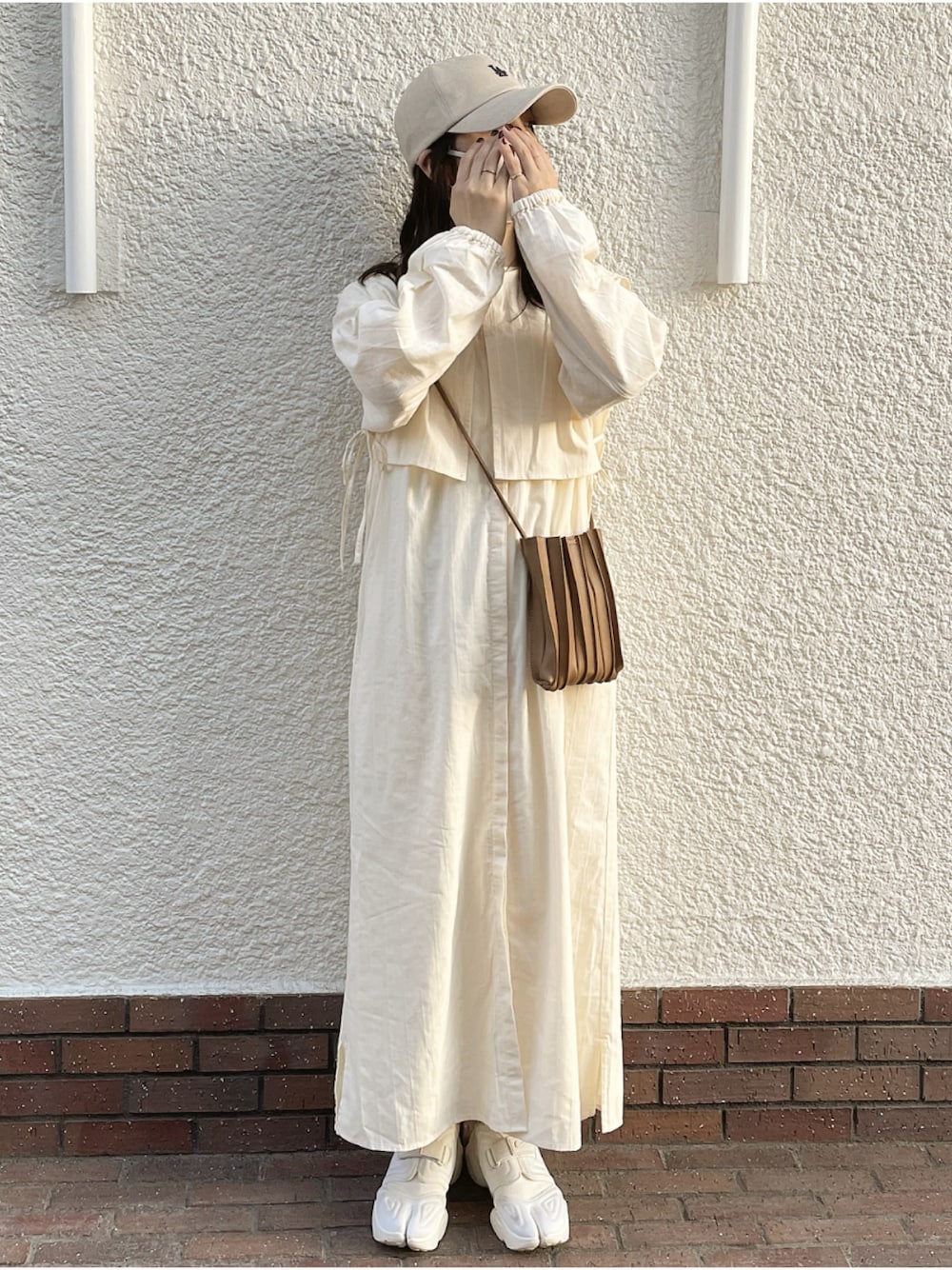 ベージュ系のワンピース、ベージュ系のショルダーバッグ、ホワイト系のスニーカーを着用したレディースの春コーディネートの1枚目の写真