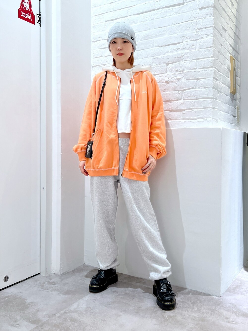 グレー系のスウェットパンツ、オレンジ系のスウェット、ホワイト系のパーカーを着用したレディースの春コーディネートの1枚目の写真