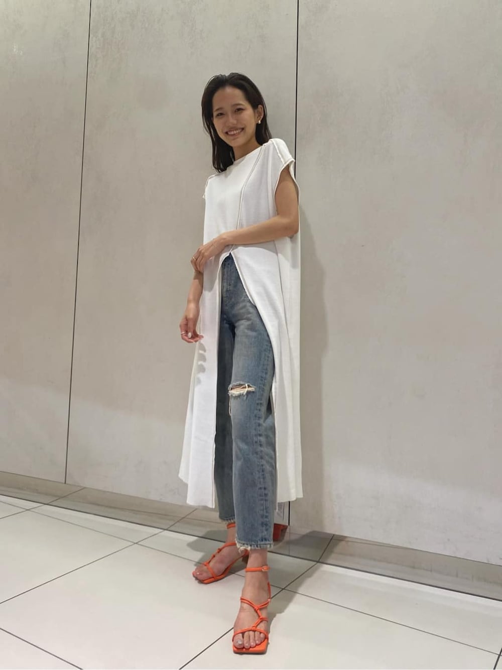 ブルー系のデニムパンツ、オレンジ系のサンダル、ホワイト系のワンピースを着用したレディースの夏コーディネートの1枚目の写真