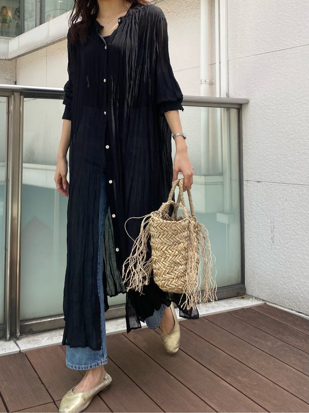 ブルー系のデニムパンツ、ブラック系のワンピース、ベージュ系のかごバッグを着用したレディースの春コーディネートの1枚目の写真