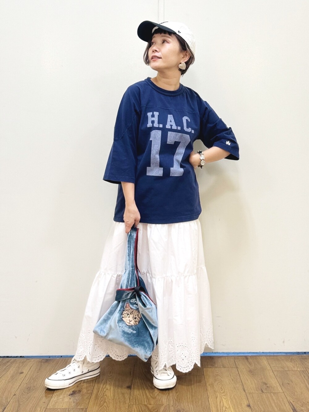 ブルー系のトートバッグ、ホワイト系のスニーカー、ホワイト系のスカートを着用したレディースの秋コーディネートの1枚目の写真