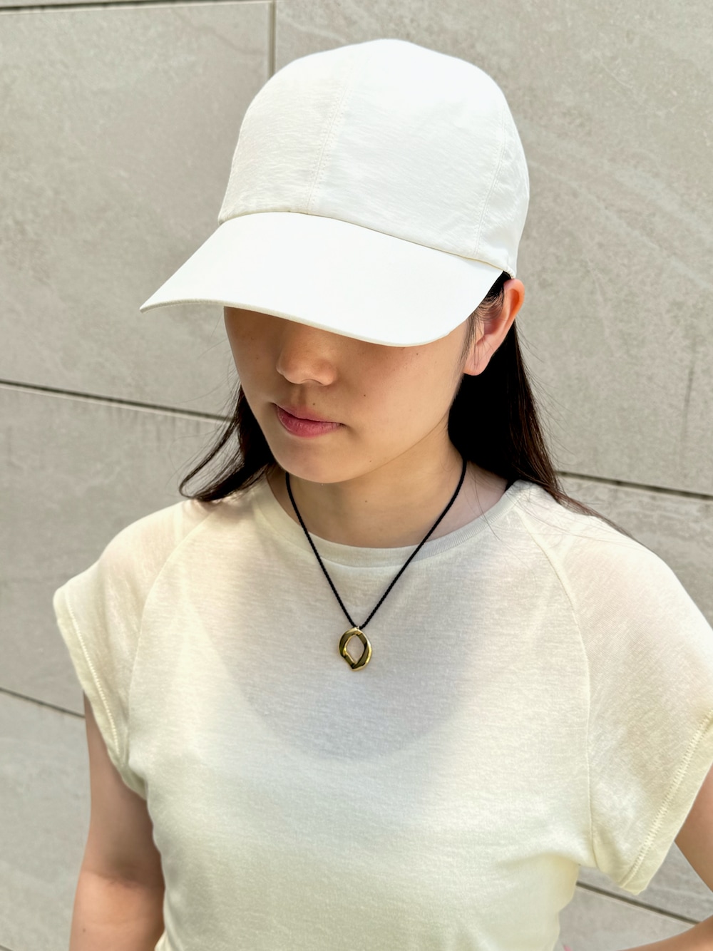 ベージュ系のTシャツ/カットソー、ホワイト系のキャップ、ゴールド系のネックレスを着用したレディースの夏コーディネートの1枚目の写真