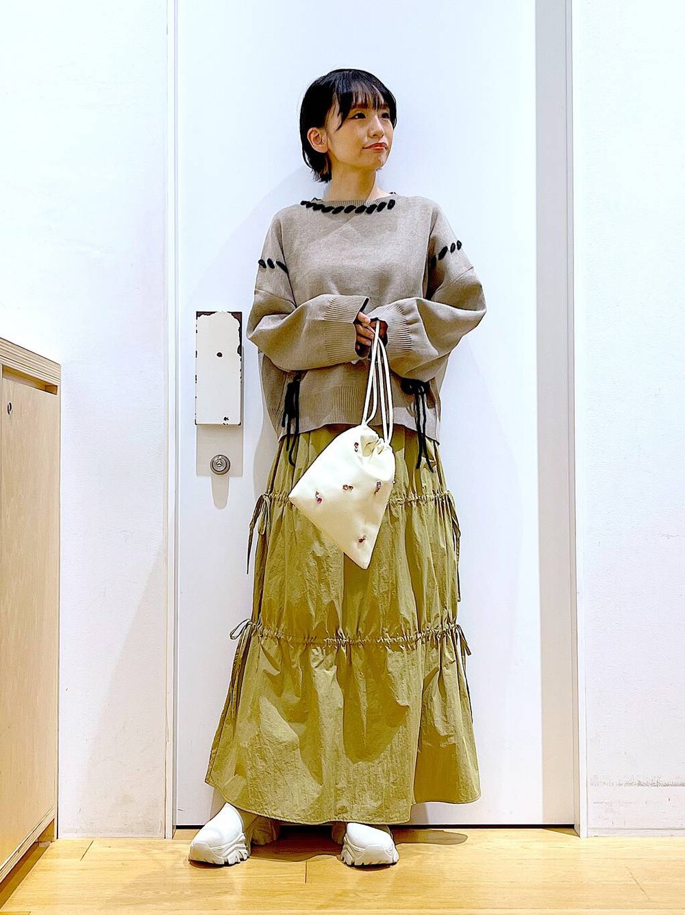 ホワイト系のショルダーバッグ、イエロー系のスカート、ベージュ系のブーツを着用したレディースの秋コーディネートの1枚目の写真