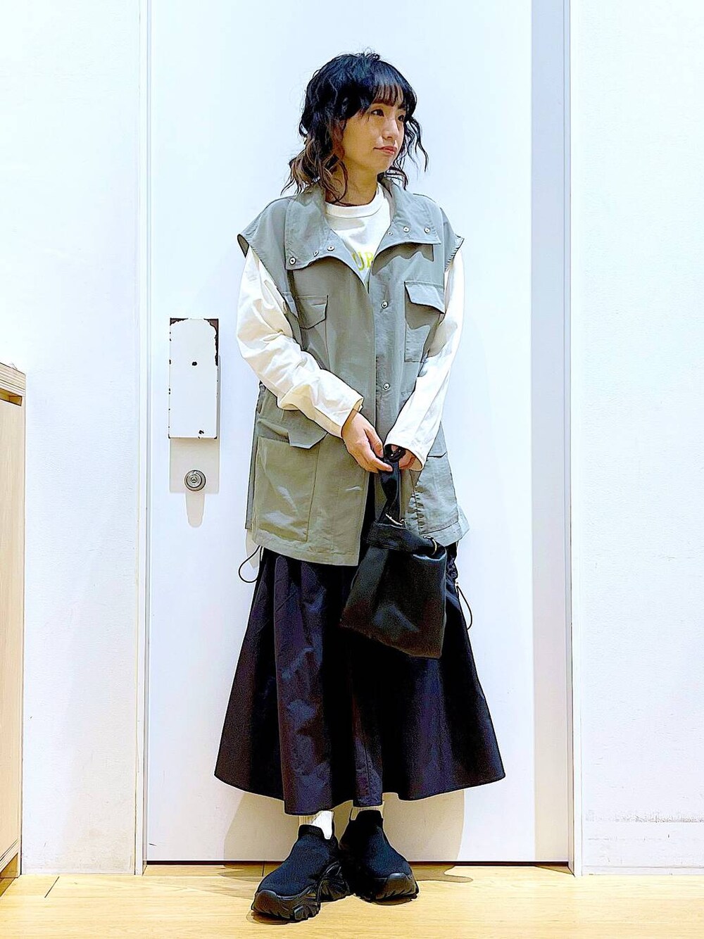 ブラック系のショルダーバッグ、ブラック系のスニーカー、ブラック系のスカートを着用したレディースの春コーディネートの1枚目の写真