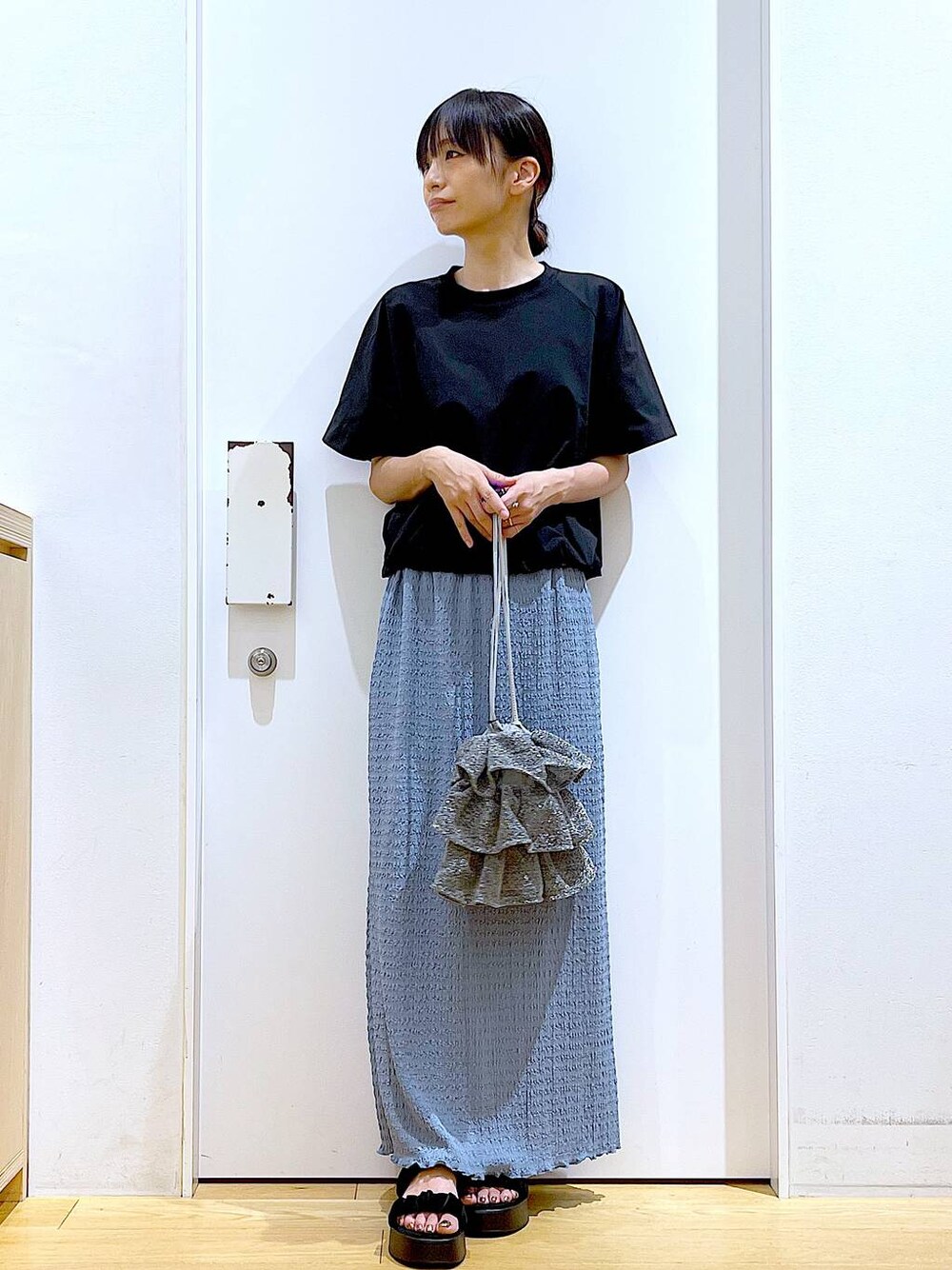 シルバー系のショルダーバッグ、ブルー系のスカート、ブラック系のTシャツ/カットソーを着用したレディースの夏コーディネートの1枚目の写真