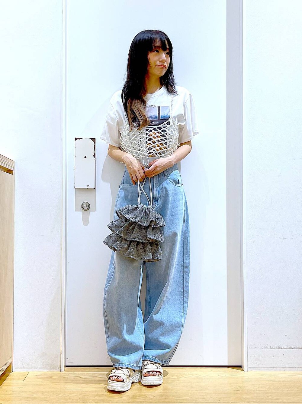 シルバー系のショルダーバッグ、ベージュ系のサンダル、ブルー系のデニムパンツを着用したレディースの夏コーディネートの1枚目の写真