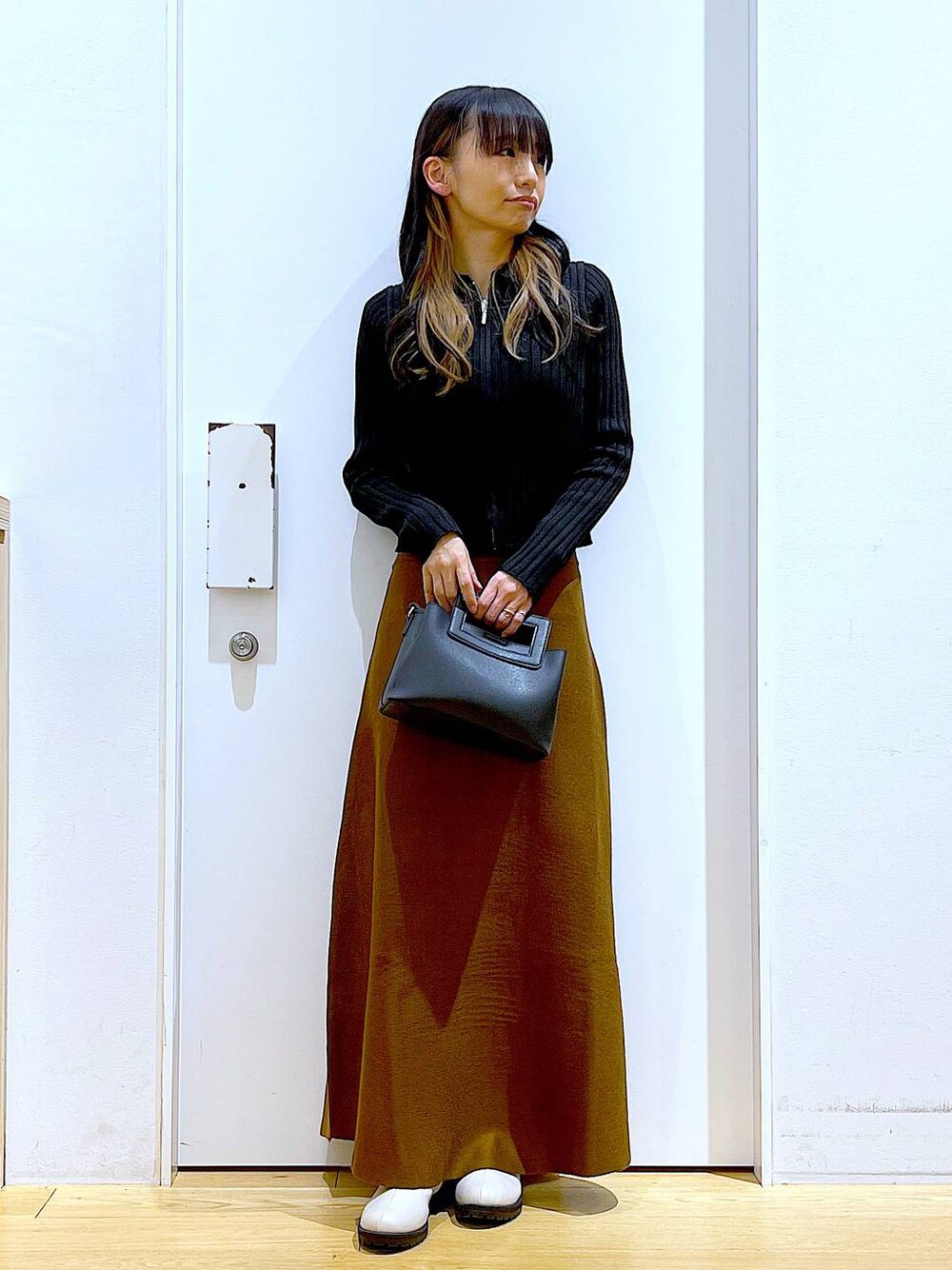 ブラック系のカーディガン/ボレロ、ブラウン系のスカート、ベージュ系のブーツを着用したレディースの冬コーディネートの1枚目の写真