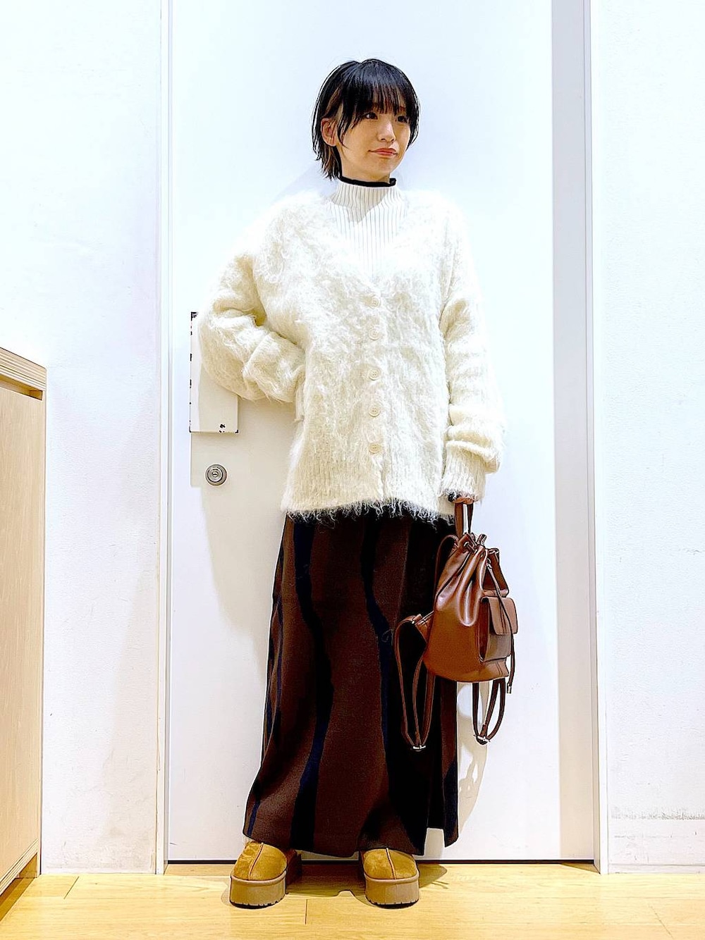 ベージュ系のニット/セーター、ブラウン系のバックパック/リュック、ブラウン系のスカートを着用したレディースの冬コーディネートの1枚目の写真