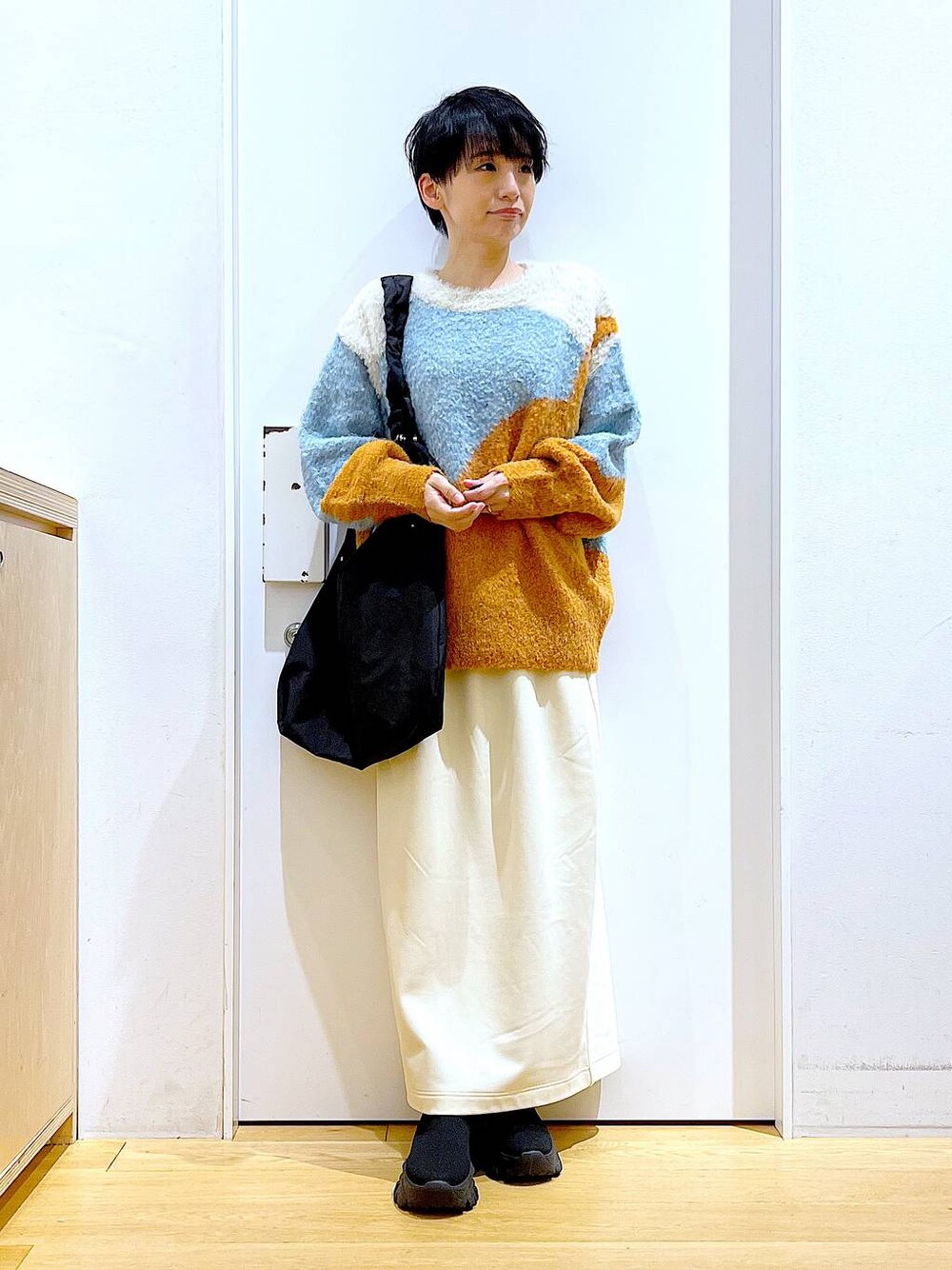 ブラック系のショルダーバッグ、ブラック系のブーツ、オレンジ系のニット/セーターを着用したレディースの冬コーディネートの1枚目の写真