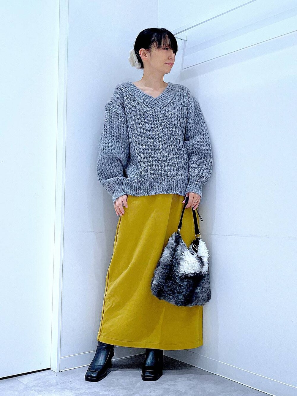 グレー系のニット/セーター、イエロー系のスカート、ブラック系のブーツを着用したレディースの冬コーディネートの1枚目の写真