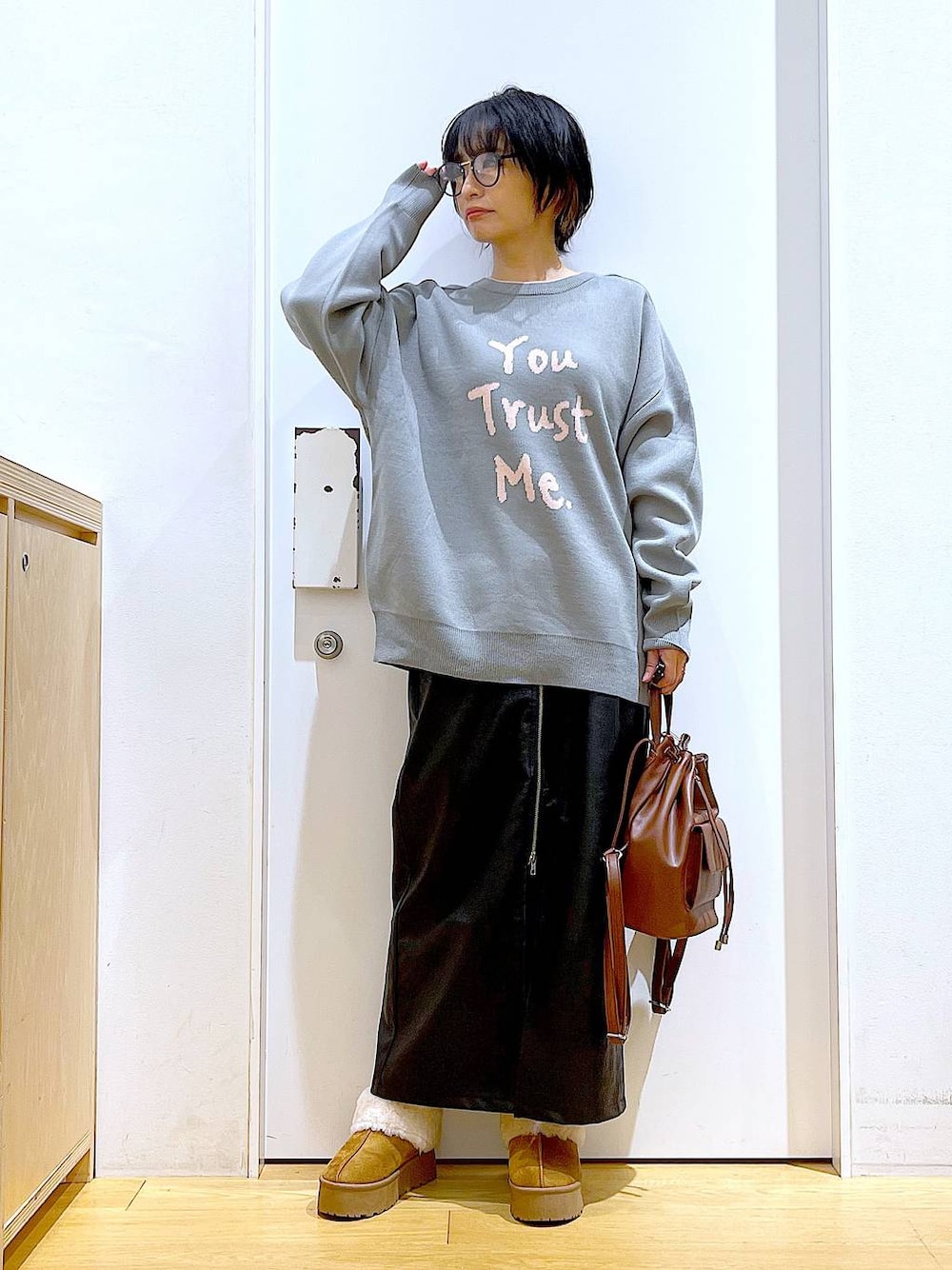 グレー系のニット/セーター、ブラウン系のバックパック/リュック、ブラック系のスカートを着用したレディースの冬コーディネートの1枚目の写真