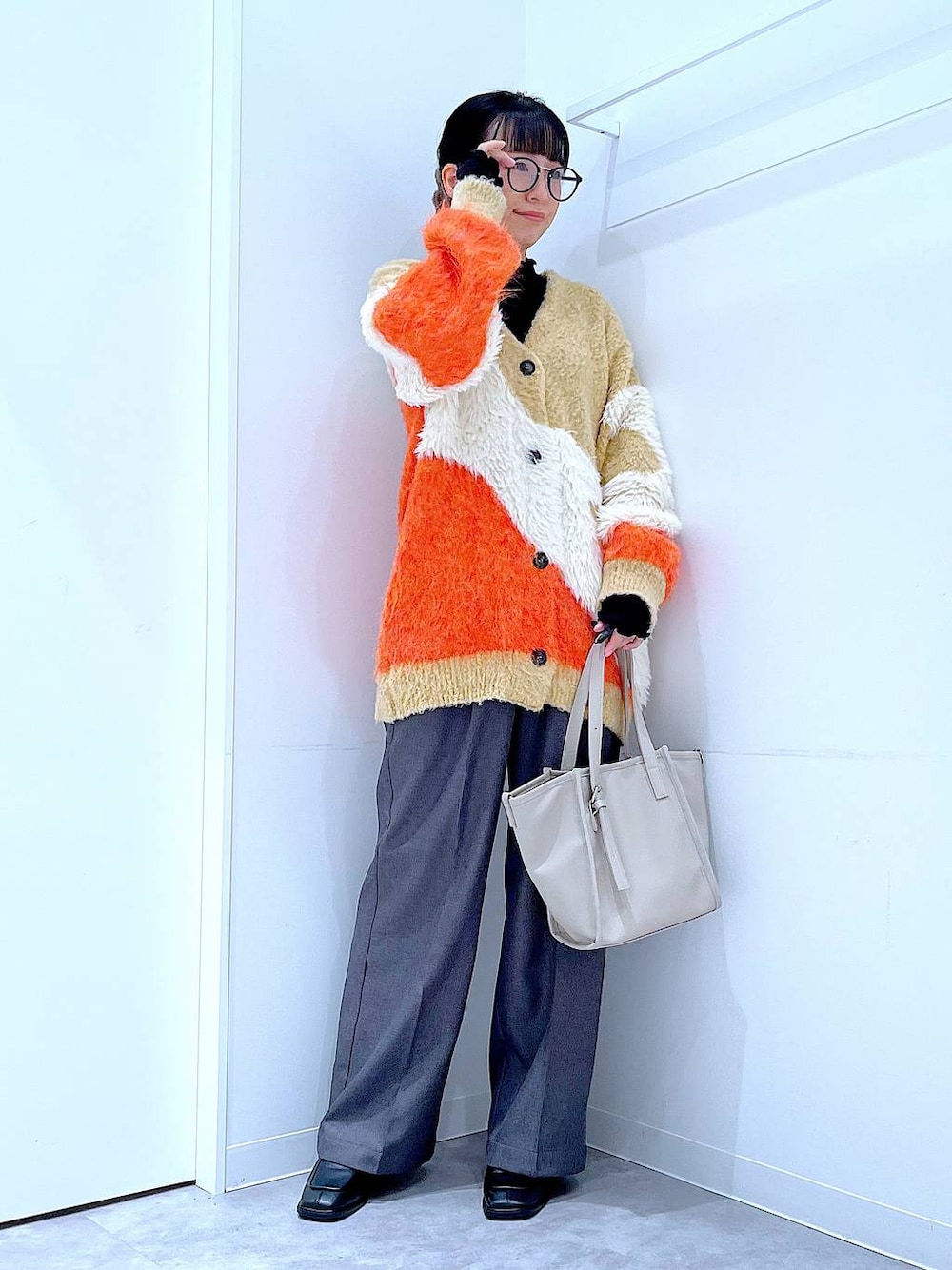 オレンジ系のカーディガン/ボレロ、ブラック系のブーツ、グレー系のスラックスを着用したレディースの冬コーディネートの1枚目の写真