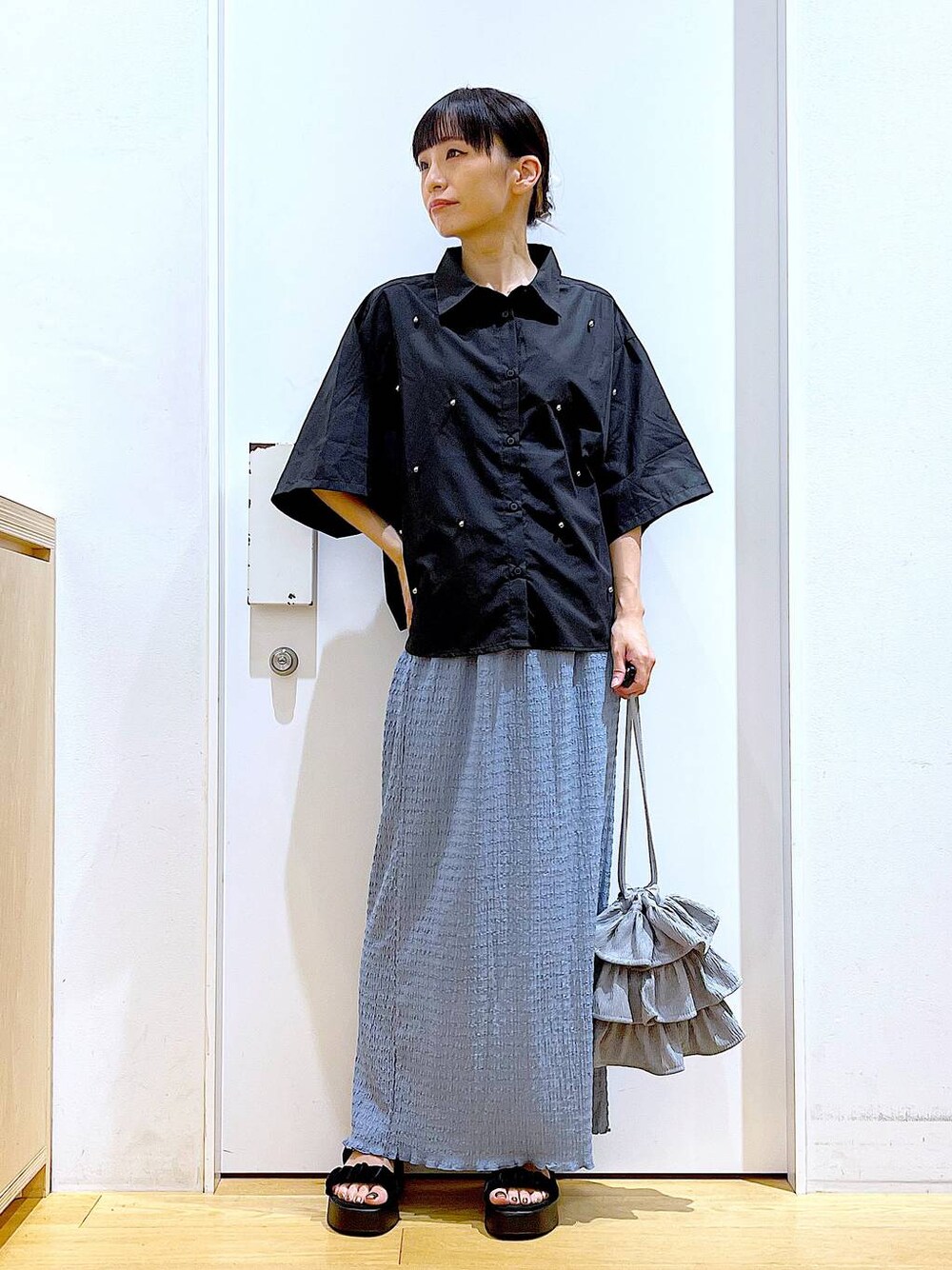 ブラック系のサンダル、ブルー系のスカート、グレー系のショルダーバッグを着用したレディースの秋コーディネートの1枚目の写真