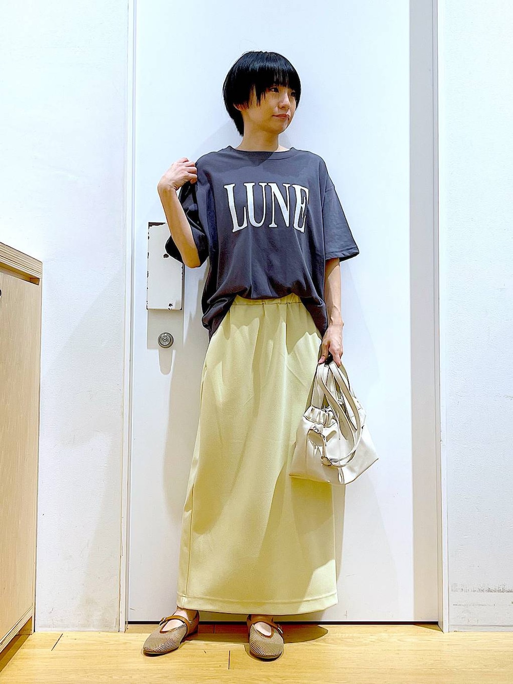 ホワイト系のショルダーバッグ、ベージュ系のパンプス、イエロー系のスカートを着用したレディースの夏コーディネートの1枚目の写真