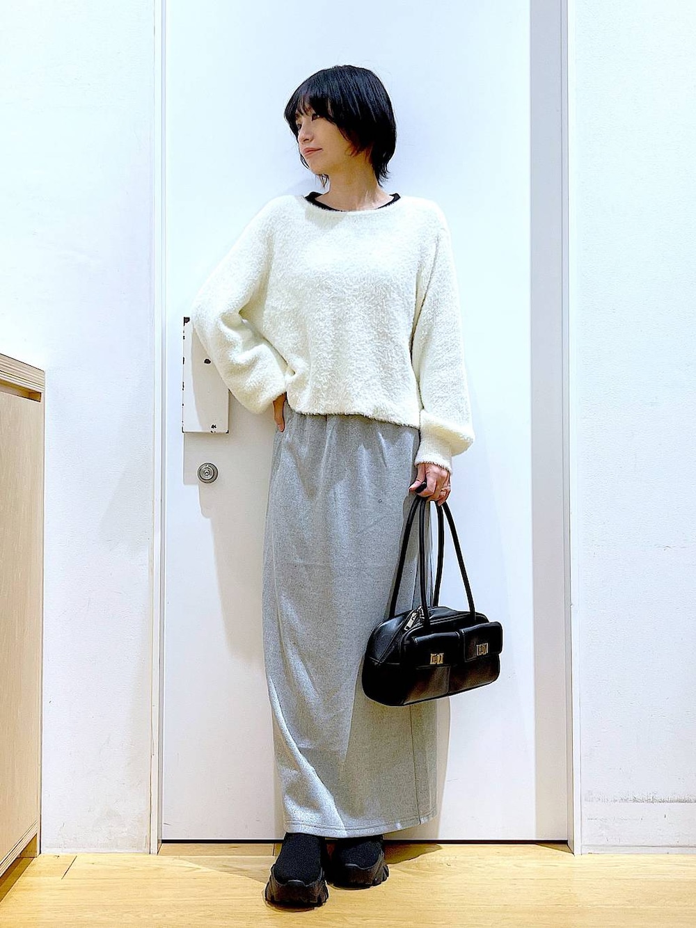 ブラック系のハンドバッグ、ブラック系のブーツ、グレー系のスカートを着用したレディースの冬コーディネートの1枚目の写真