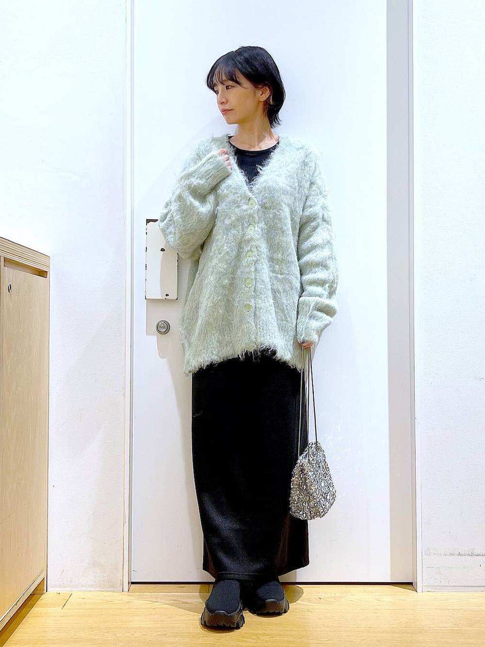 グリーン系のカーディガン/ボレロ、ブラック系のブーツ、ブラック系のスカートを着用したレディースの冬コーディネートの1枚目の写真