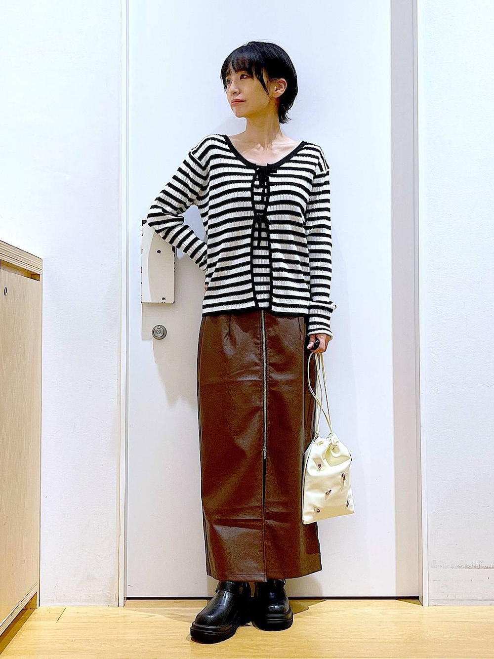 ブラウン系のスカート、ホワイト系のショルダーバッグ、ブラック系のブーツを着用したレディースの秋コーディネートの1枚目の写真