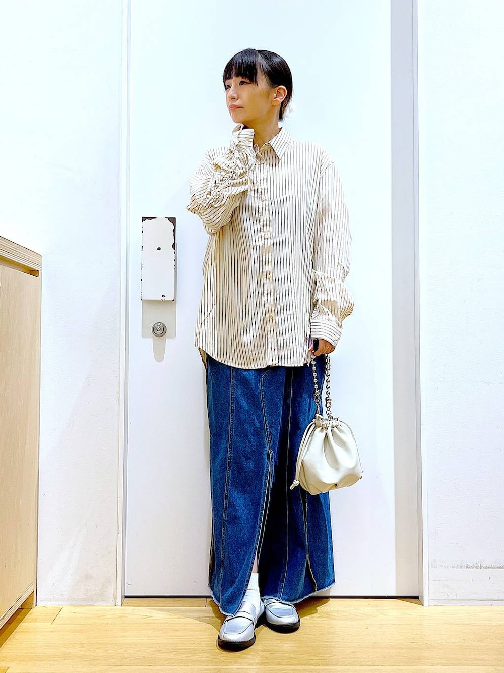 ベージュ系のショルダーバッグ、シルバー系のローファー、ブルー系のデニムスカートを着用したレディースの秋コーディネートの1枚目の写真