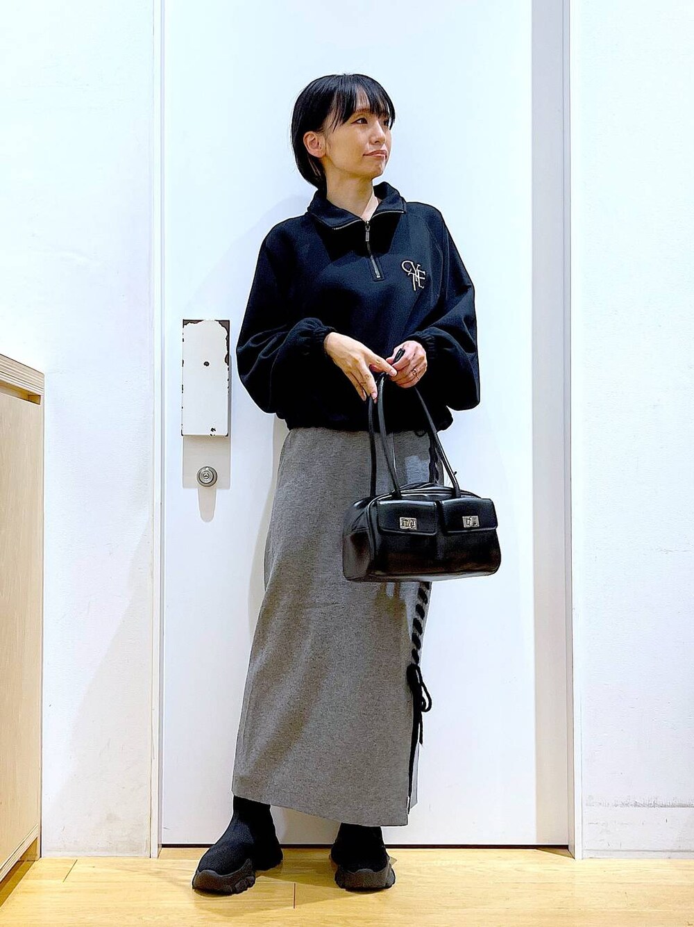 ブラック系のハンドバッグ、ブラック系のブーツ、グレー系のスカートを着用したレディースの冬コーディネートの1枚目の写真