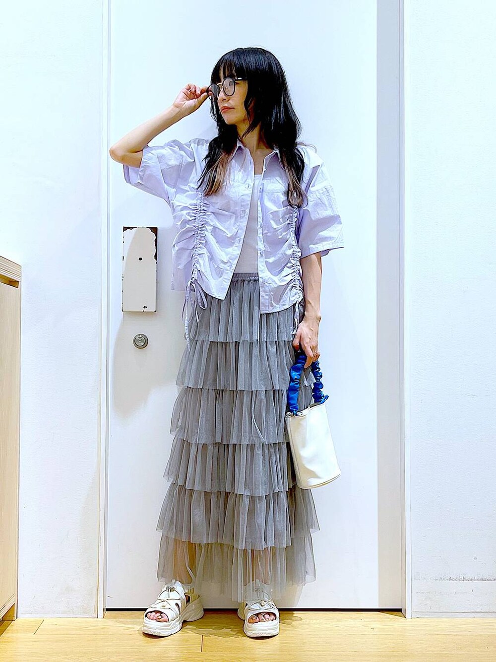 ブルー系のショルダーバッグ、ホワイト系のサンダル、グレー系のスカートを着用したレディースの夏コーディネートの1枚目の写真