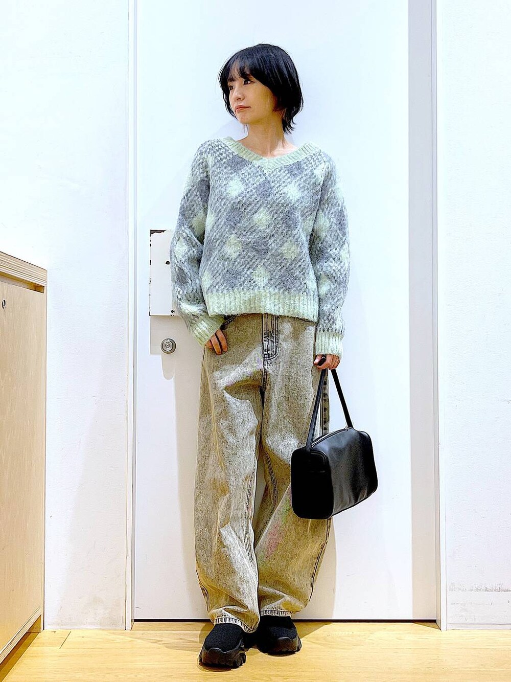 ブラック系のショルダーバッグ、ブラック系のブーツ、ベージュ系のデニムパンツを着用したレディースの冬コーディネートの1枚目の写真