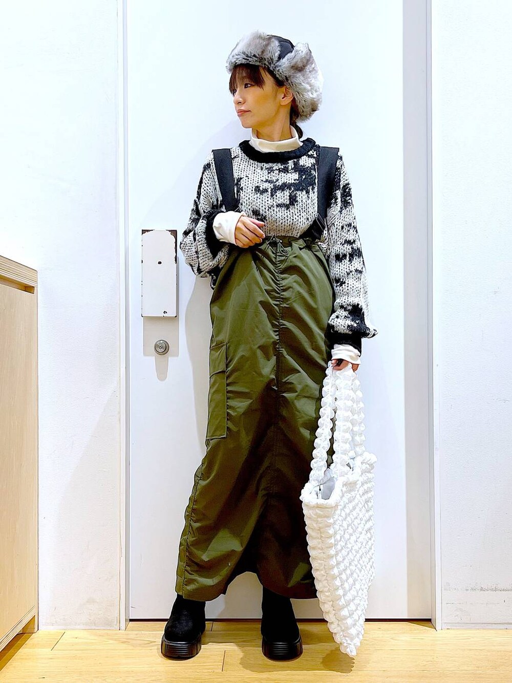 ホワイト系のトートバッグ、ベージュ系のTシャツ/カットソー、グリーン系のジャンパースカートを着用したレディースの冬コーディネートの1枚目の写真