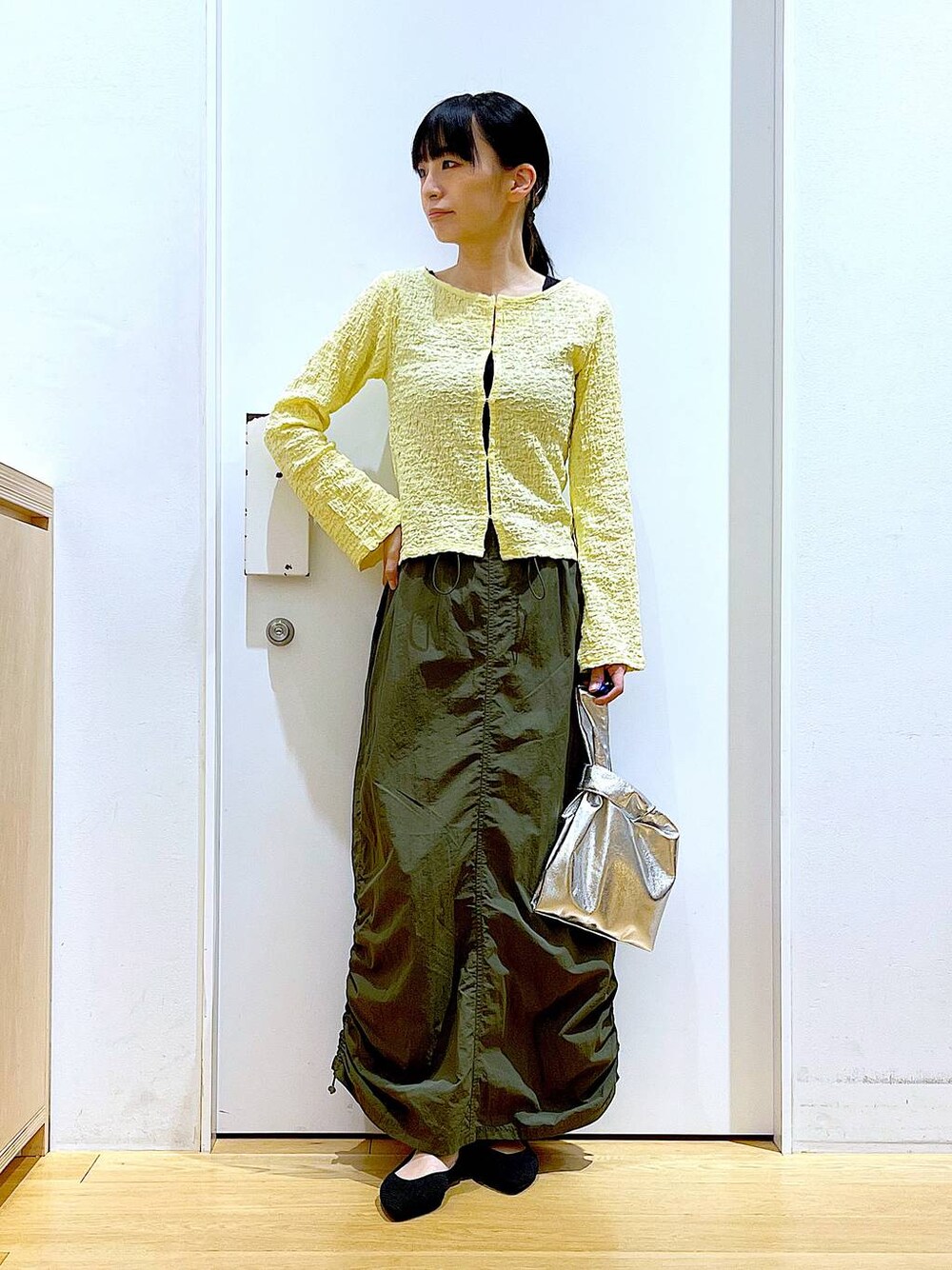 シルバー系のショルダーバッグ、グリーン系のスカート、ブラック系のパンプスを着用したレディースの春コーディネートの1枚目の写真