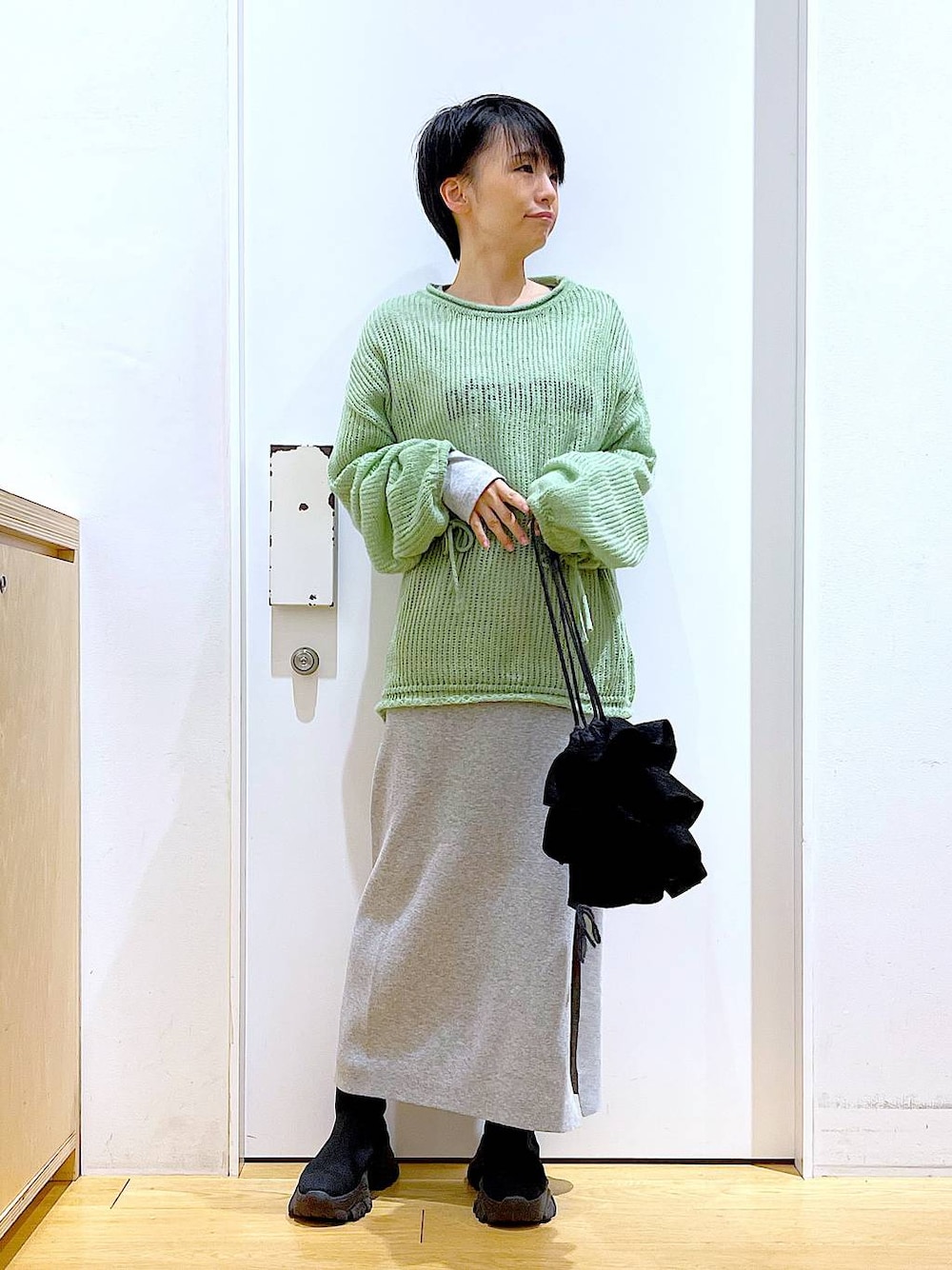 ブラック系のブーツ、グリーン系のニット/セーター、グレー系のスカートを着用したレディースの冬コーディネートの1枚目の写真