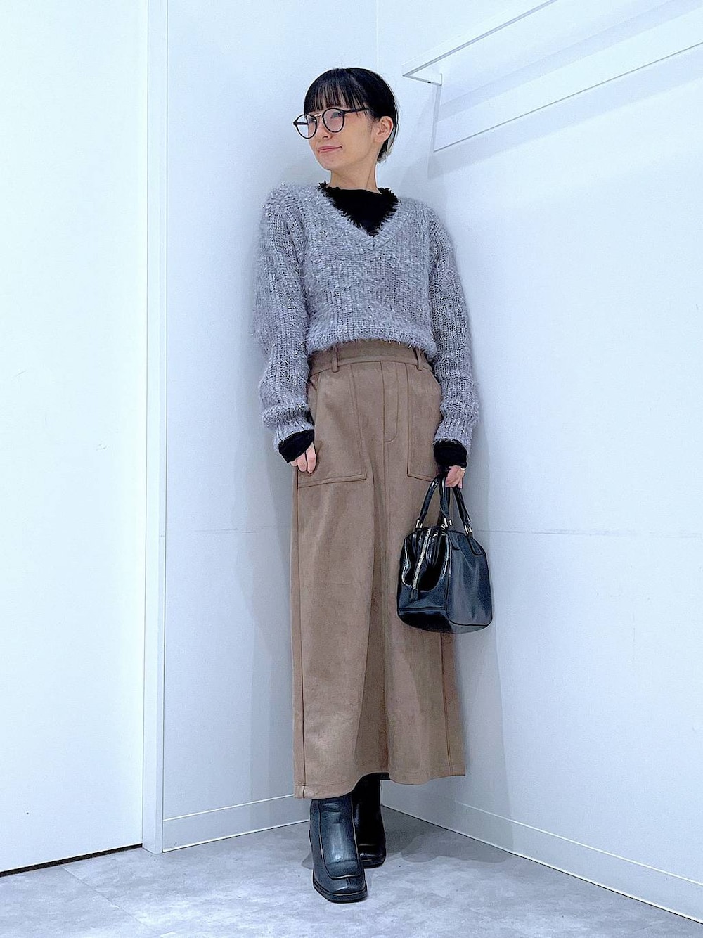 ブラック系のブーツ、ブラック系のショルダーバッグ、ブラウン系のスカートを着用したレディースの冬コーディネートの1枚目の写真