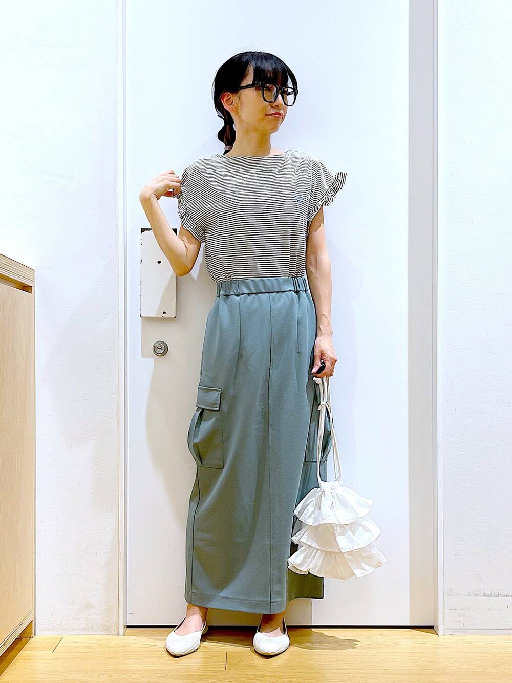 ホワイト系のショルダーバッグ、ホワイト系のパンプス、グリーン系のスカートを着用したレディースの春コーディネートの1枚目の写真