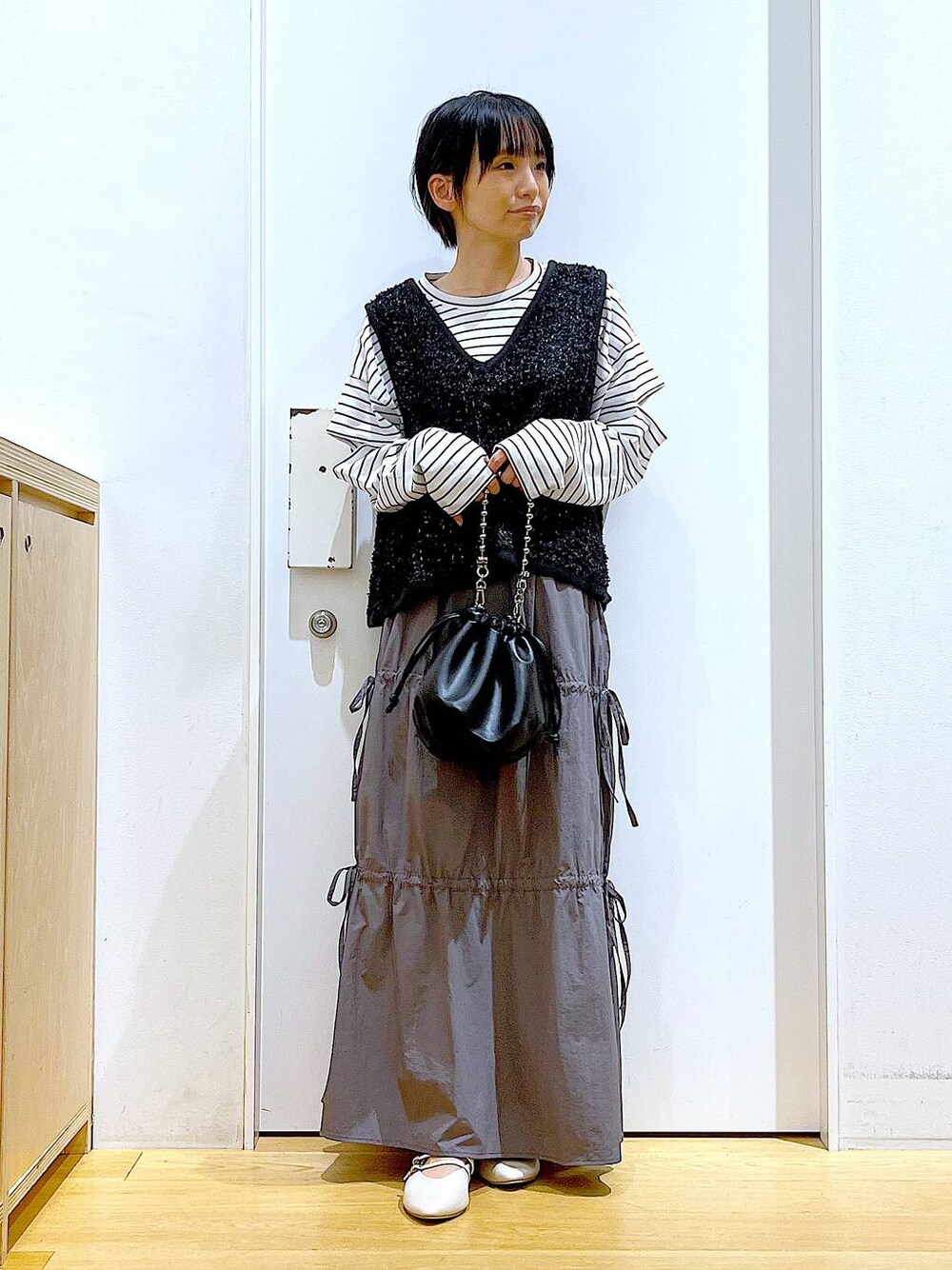 ブラック系のショルダーバッグ、ホワイト系のパンプス、グレー系のスカートを着用したレディースの秋コーディネートの1枚目の写真