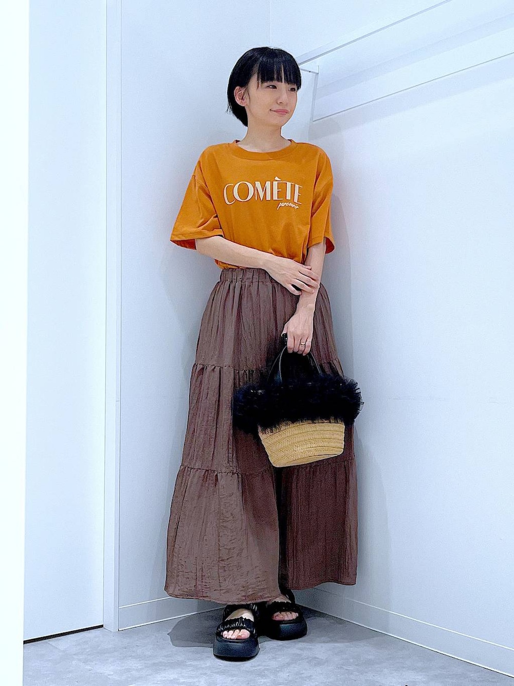 ベージュ系のショルダーバッグ、ブラック系のサンダル、オレンジ系のTシャツ/カットソーを着用したレディースの夏コーディネートの1枚目の写真