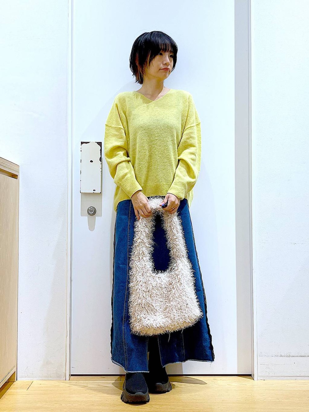 イエロー系のニット/セーター、ブルー系のデニムスカート、ベージュ系のショルダーバッグを着用したレディースの冬コーディネートの1枚目の写真