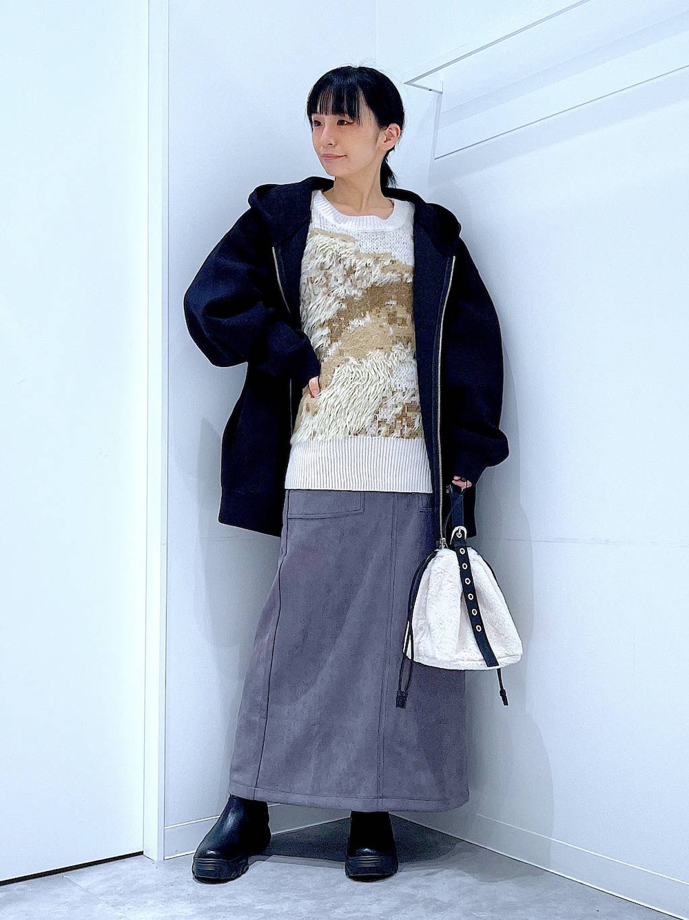 ホワイト系のハンドバッグ、ブラック系のブーツ、グレー系のスカートを着用したレディースの冬コーディネートの1枚目の写真