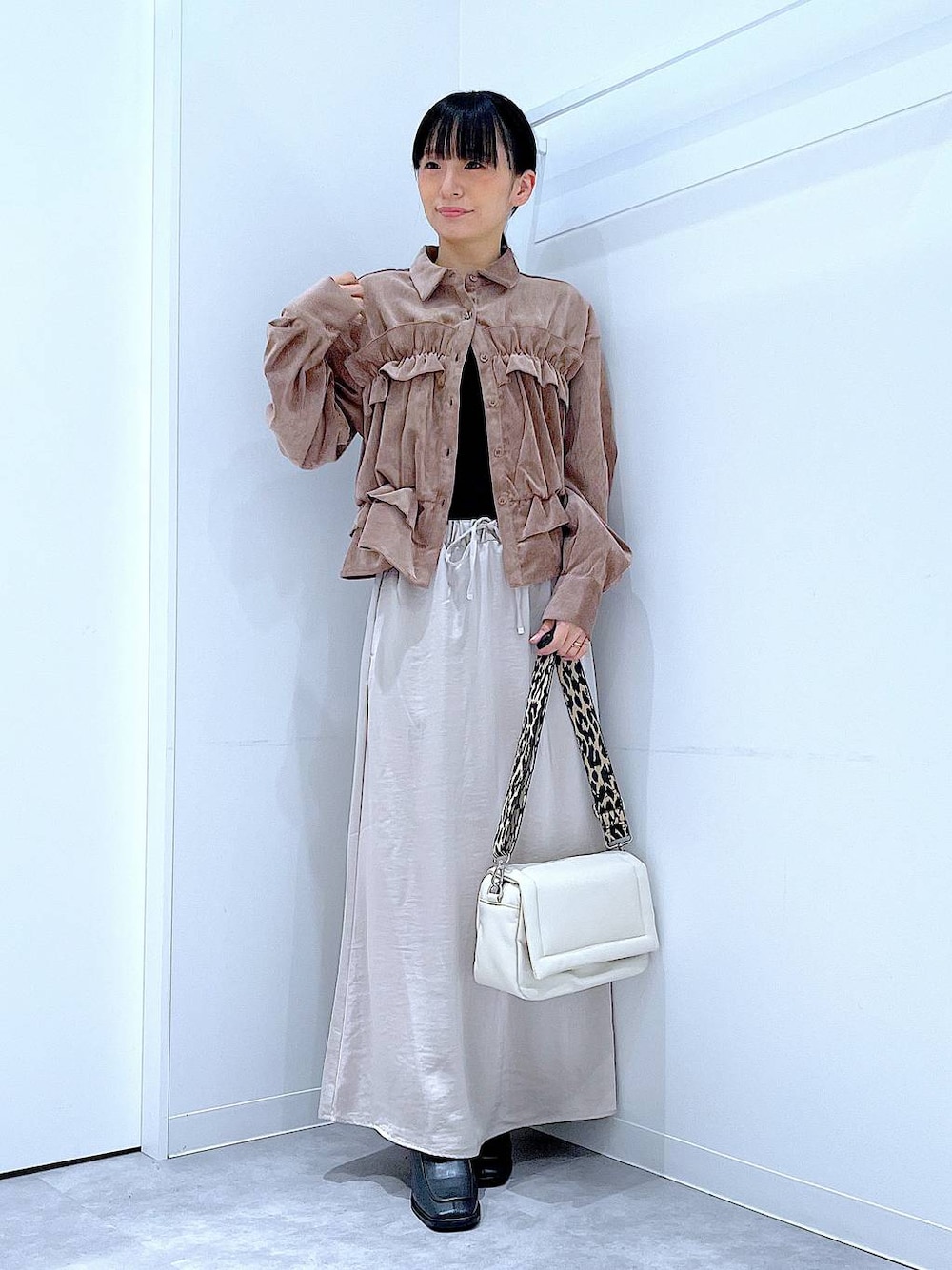 ベージュ系のスカート、ホワイト系のショルダーバッグ、ブラック系のブーツを着用したレディースの秋コーディネートの1枚目の写真